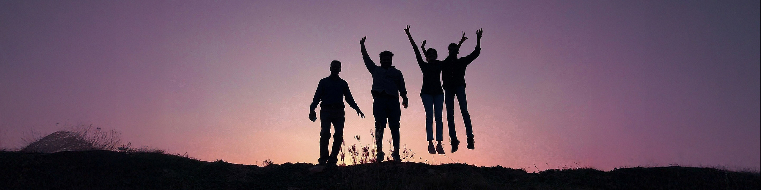 people jumoing at the top of a mountain during sunset