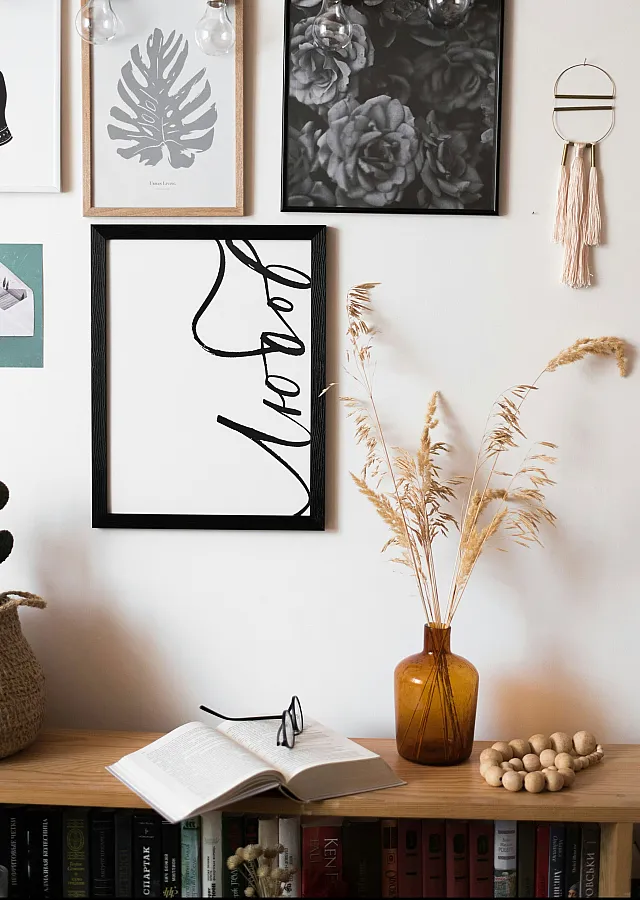 bookcase with open book and glasses and decorative items and print frames on the wall