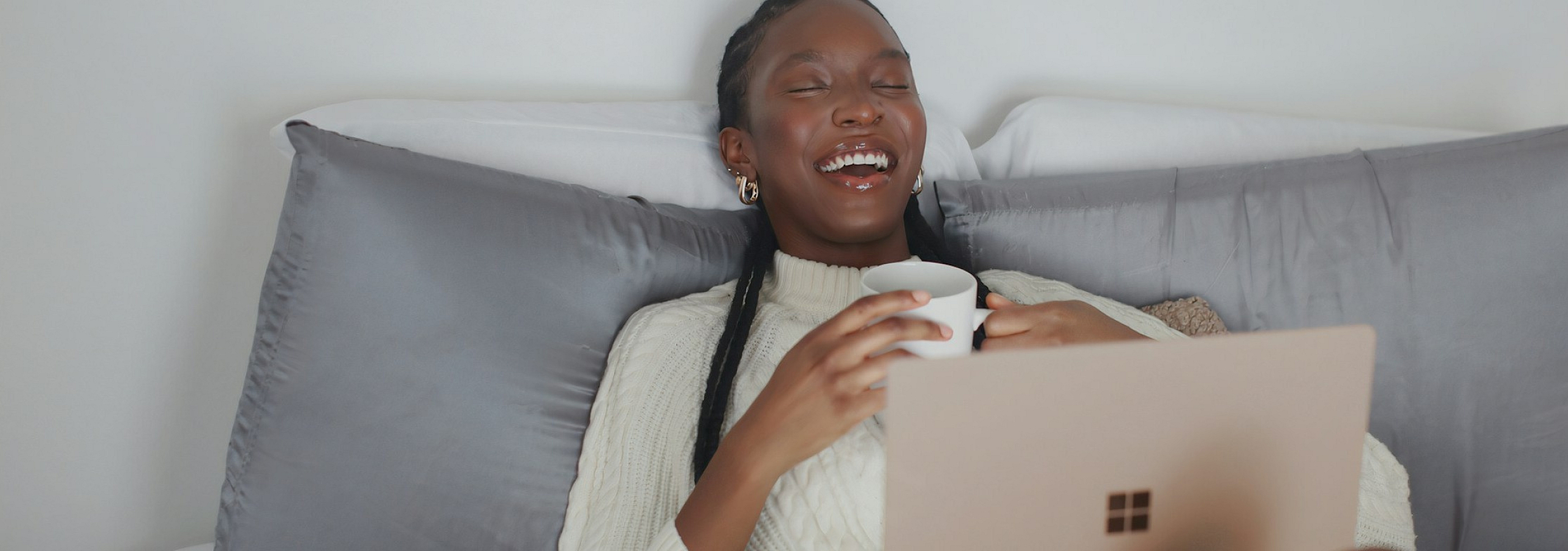 woman with a coffee mug on her laptop in bed