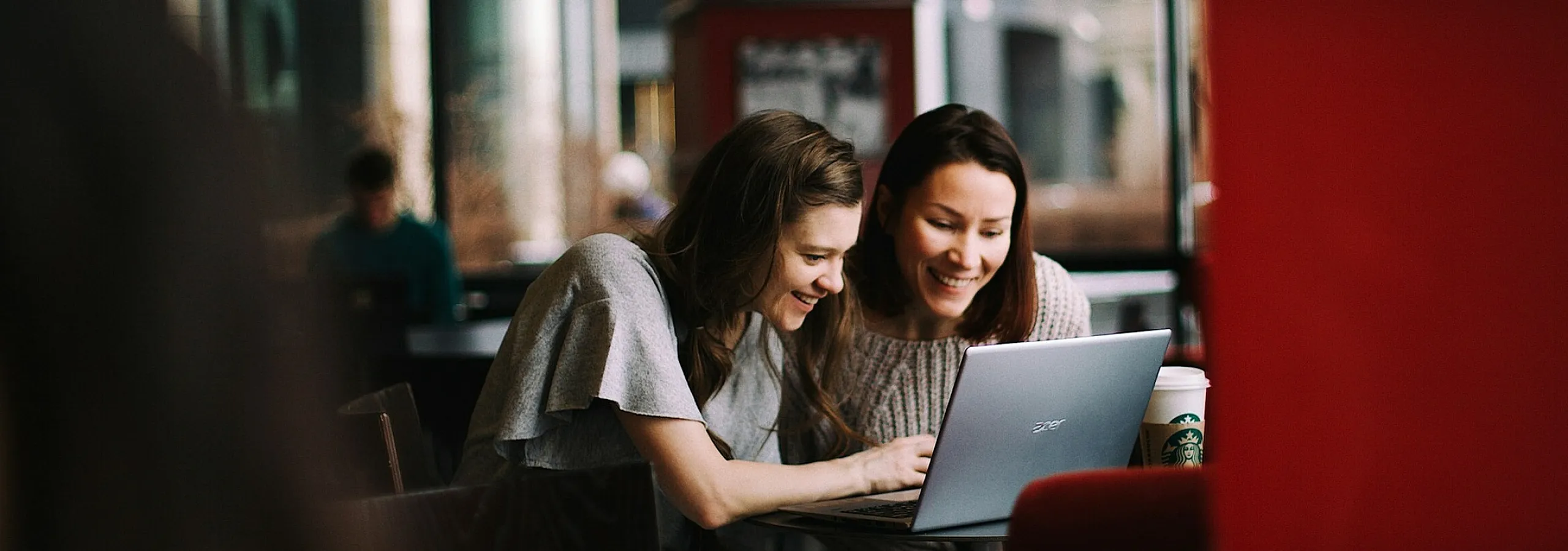 two women looking at a laptop screen at a coffee shop