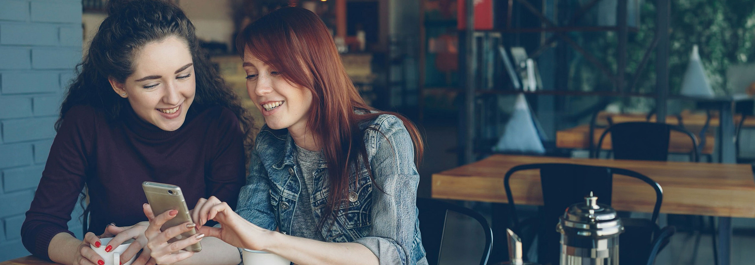 two women looking at a phone in a cafe