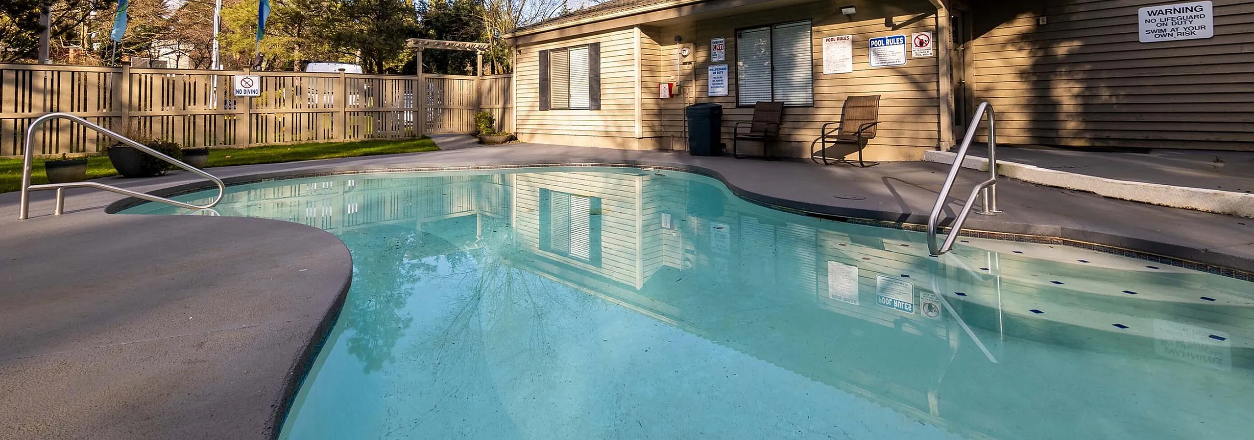 Curved outdoor pool area surrounded by tall trees and fencing at Creekwood Apartments.