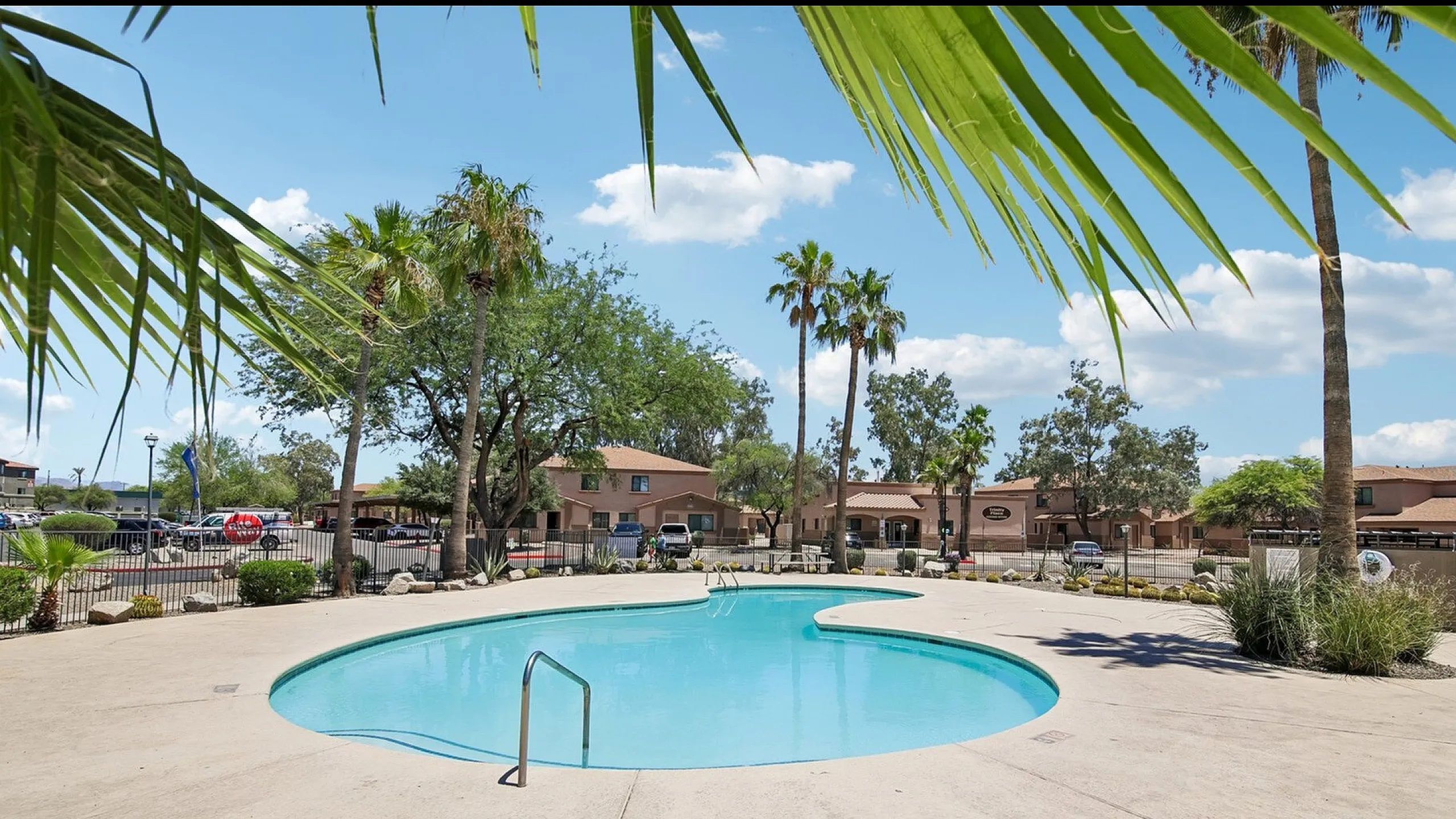 pool with three palm trees in the background and three story apartment buildings further back