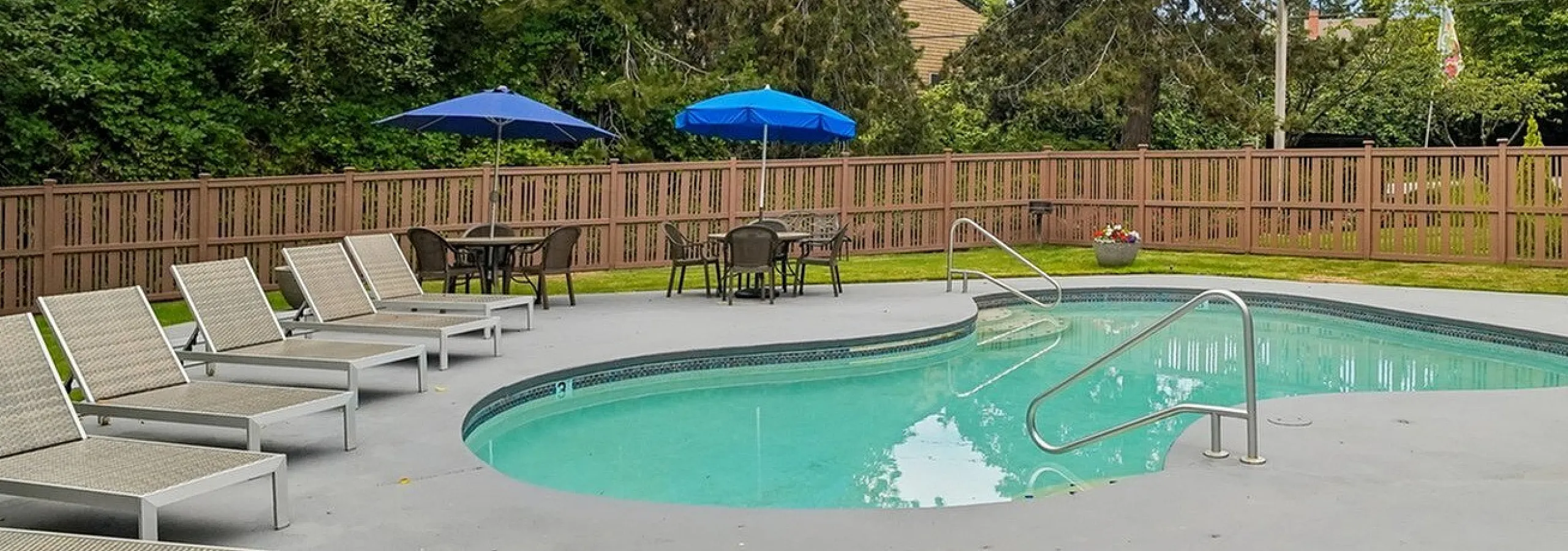 Curved outdoor pool area surrounded by tall trees and fencing at Creekwood Apartments.