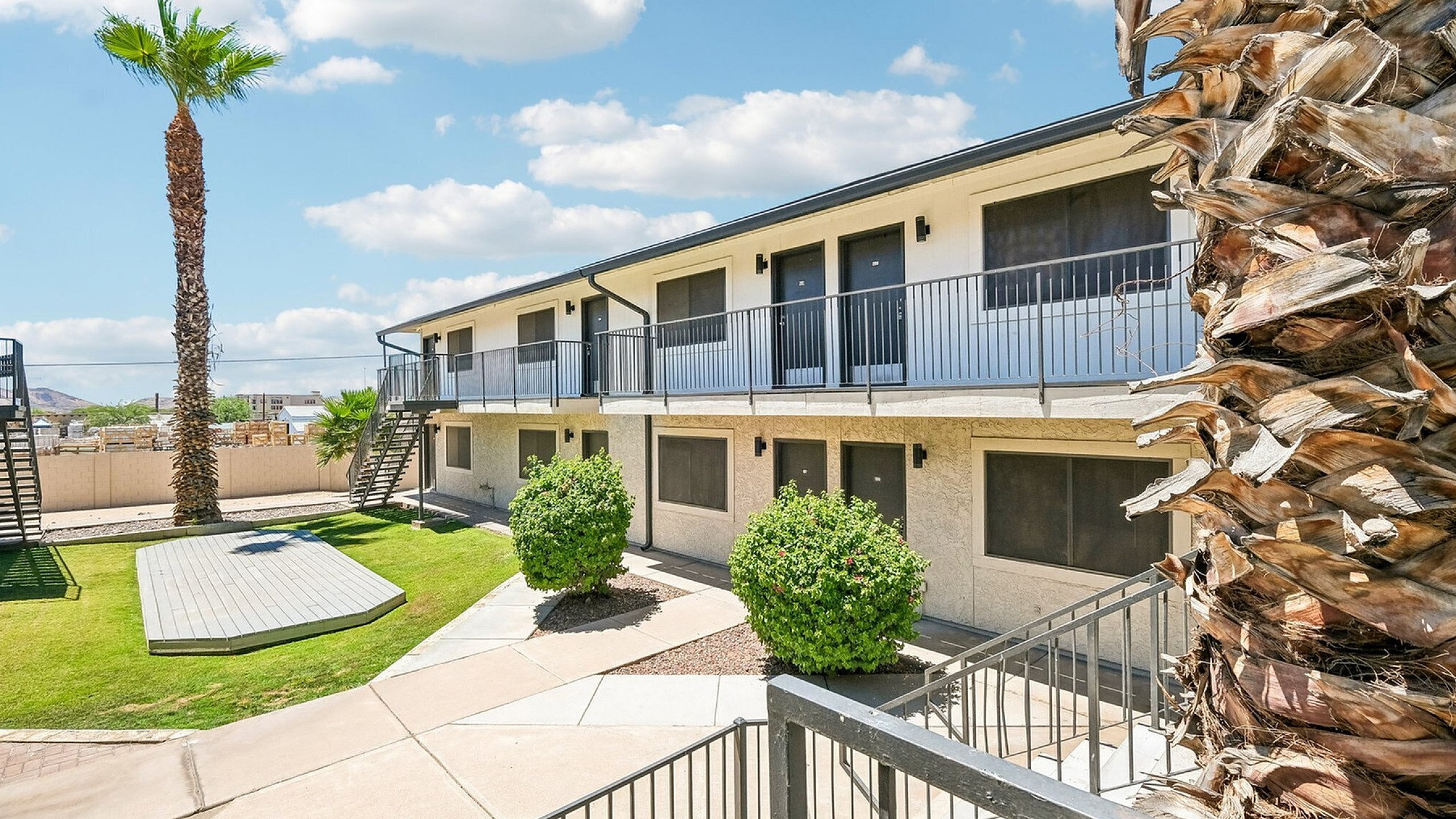 Two-story apartment building at Deer Valley Village with palm trees and metal staircases.