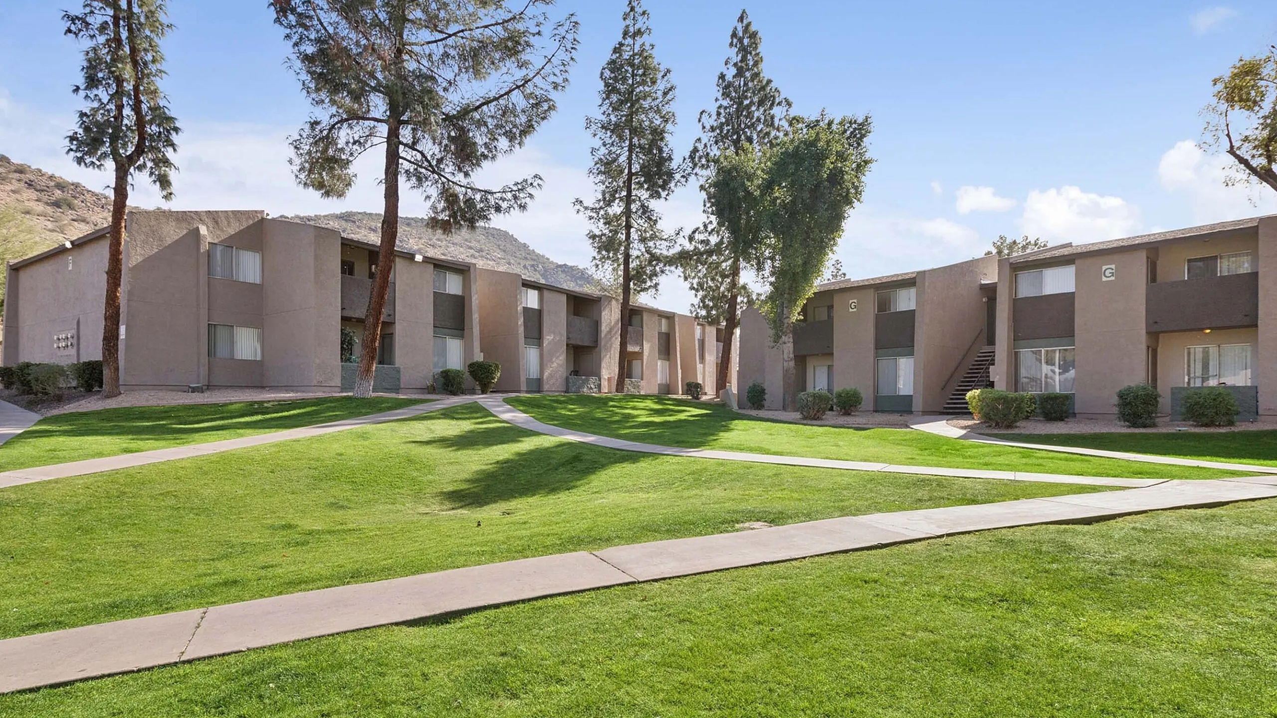 Lush green courtyard and walking paths at Solaris at Shadow Mountain under a clear blue sky.