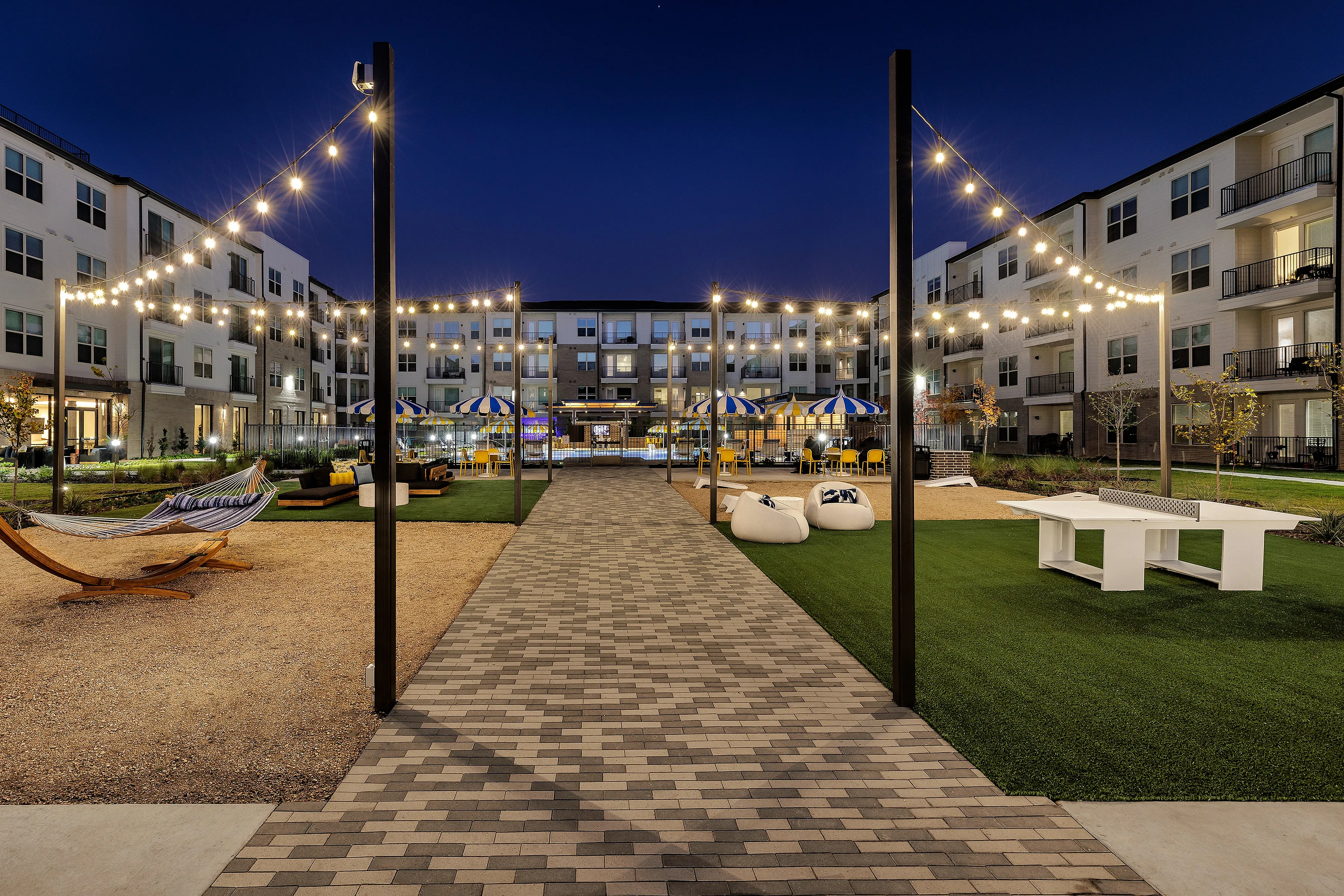 Elegant apartment courtyard with twinkling string lights, outdoor seating, and recreational amenities at night.