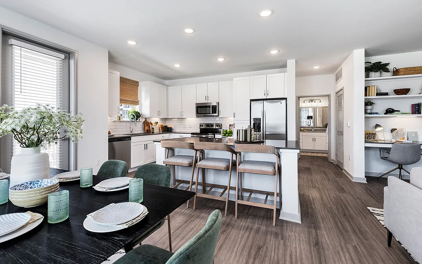 Modern open-concept kitchen with sleek white cabinetry, stainless steel appliances, and a stylish dining setup with a black table and velvet chairs.
