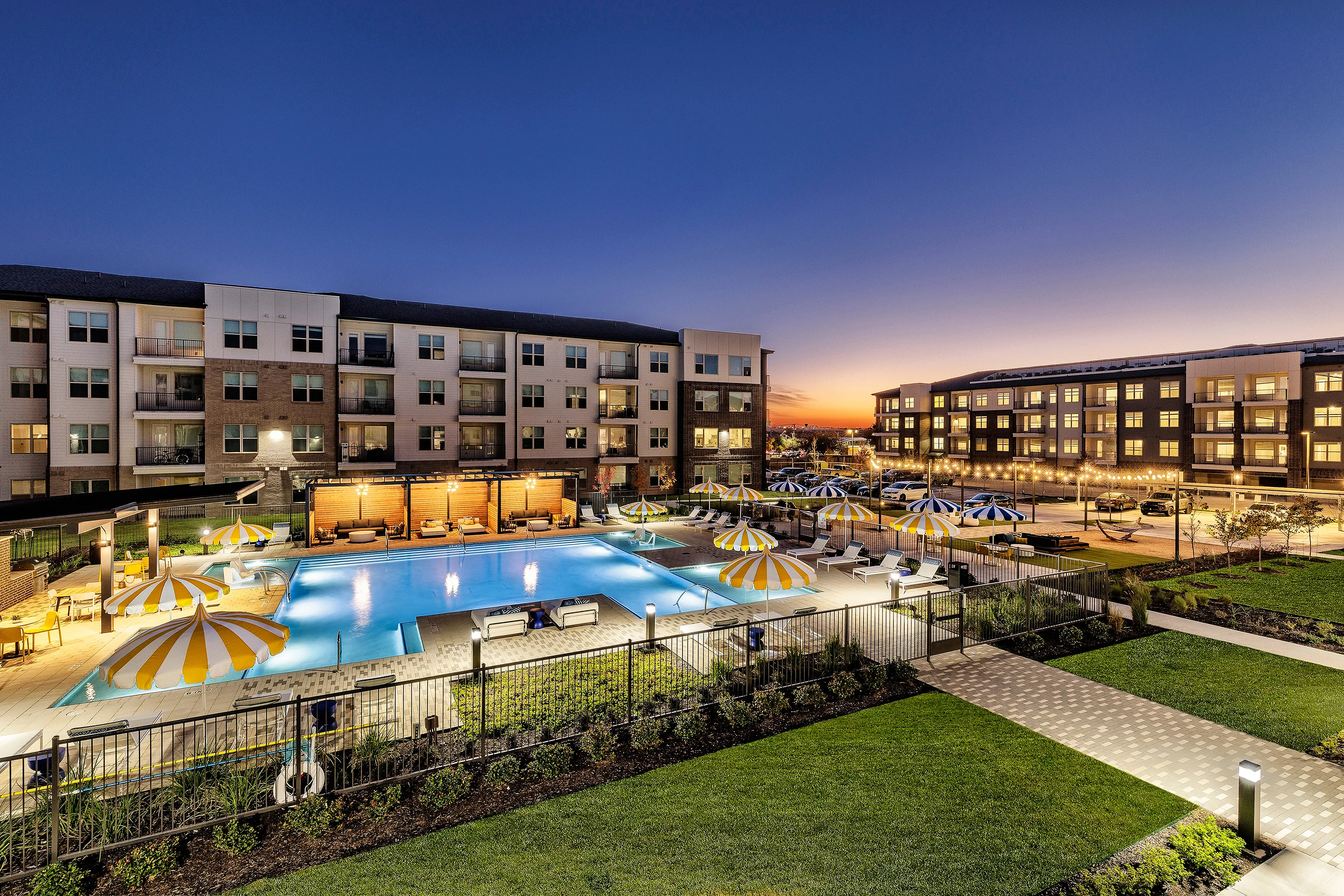 Beautiful luxury apartment complex with a sparkling pool and charming outdoor umbrellas at sunset.
