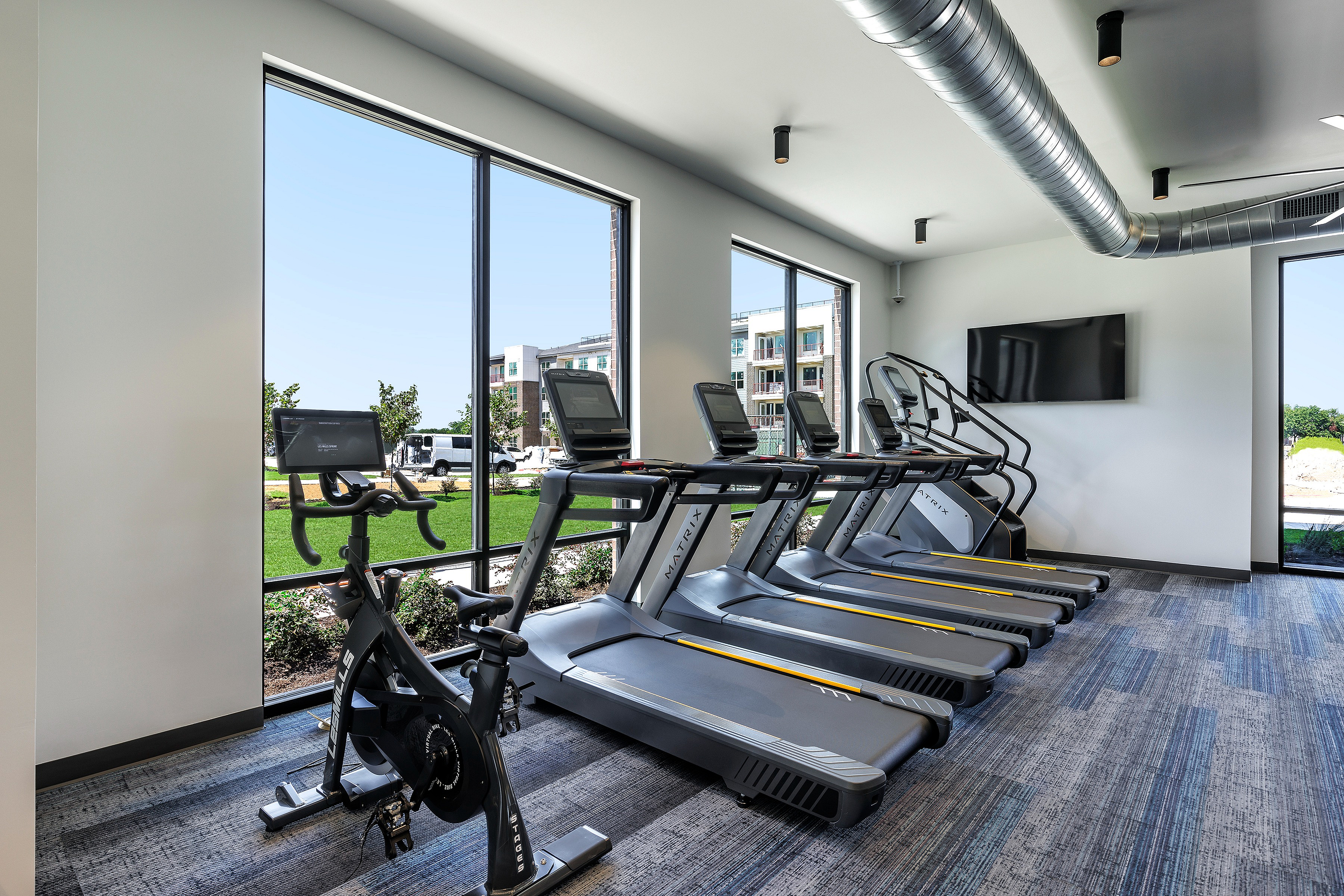 Modern fitness center with treadmills and a stationary bike, featuring expansive windows with a view of a green landscape.