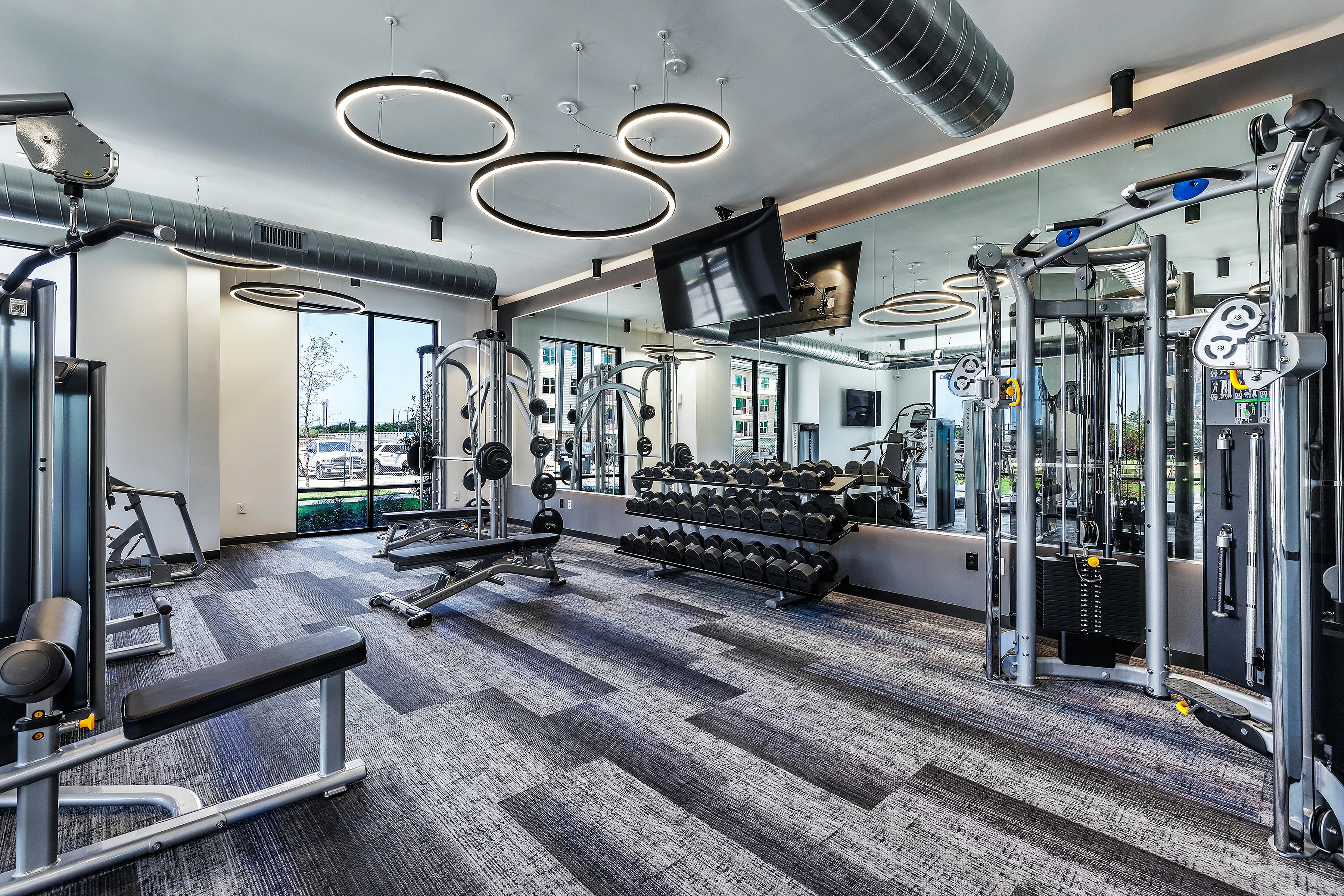 Sophisticated gym with modern equipment, stylish lighting, and large mirrors, offering a bright workout environment.