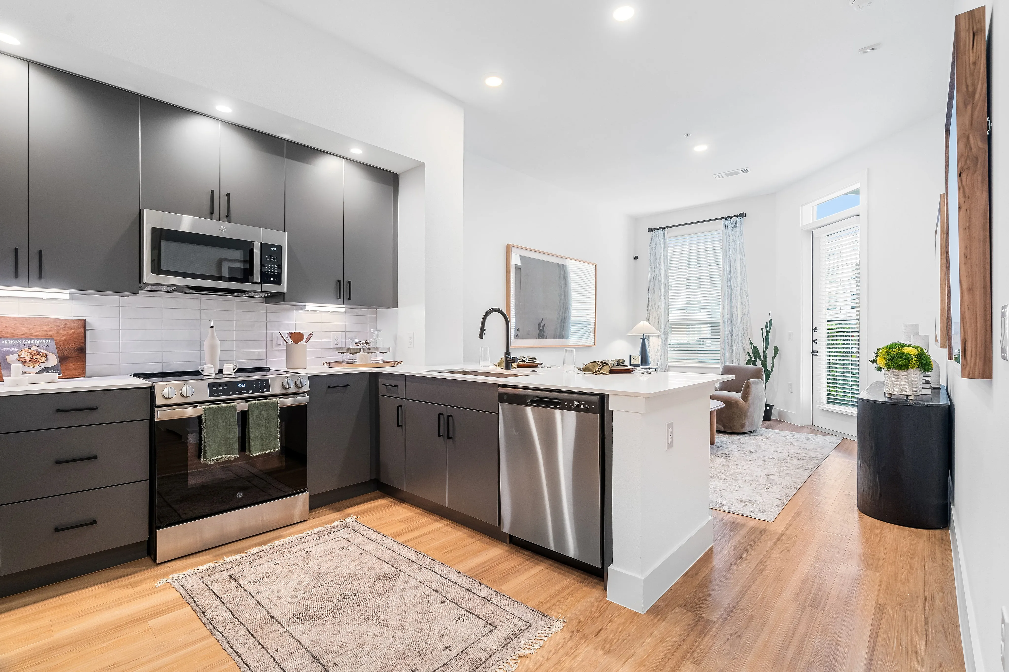 houston apartments | apartments near memorial city | apartments zoned to Katy ISD | apartments near hwy6 |Modern kitchen with sleek gray cabinetry, high-end appliances, and a cozy dining area leading to a sunlit living space with large windows.