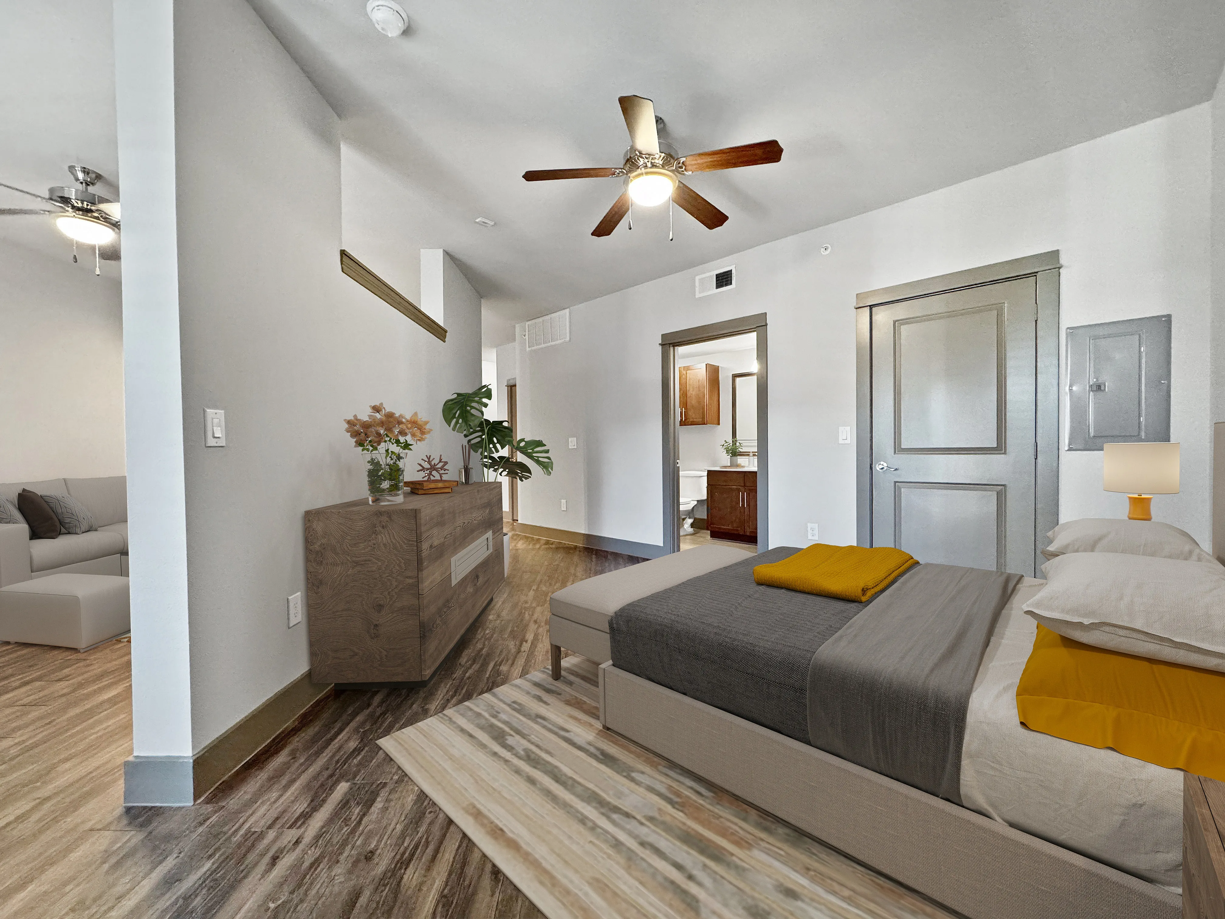 Modern apartment interior with elegant bedroom featuring stylish decor, wooden flooring, and ceiling fan. Spacious open-concept design with visible living area in neutral tones. Appealing entryway with contemporary furniture.
