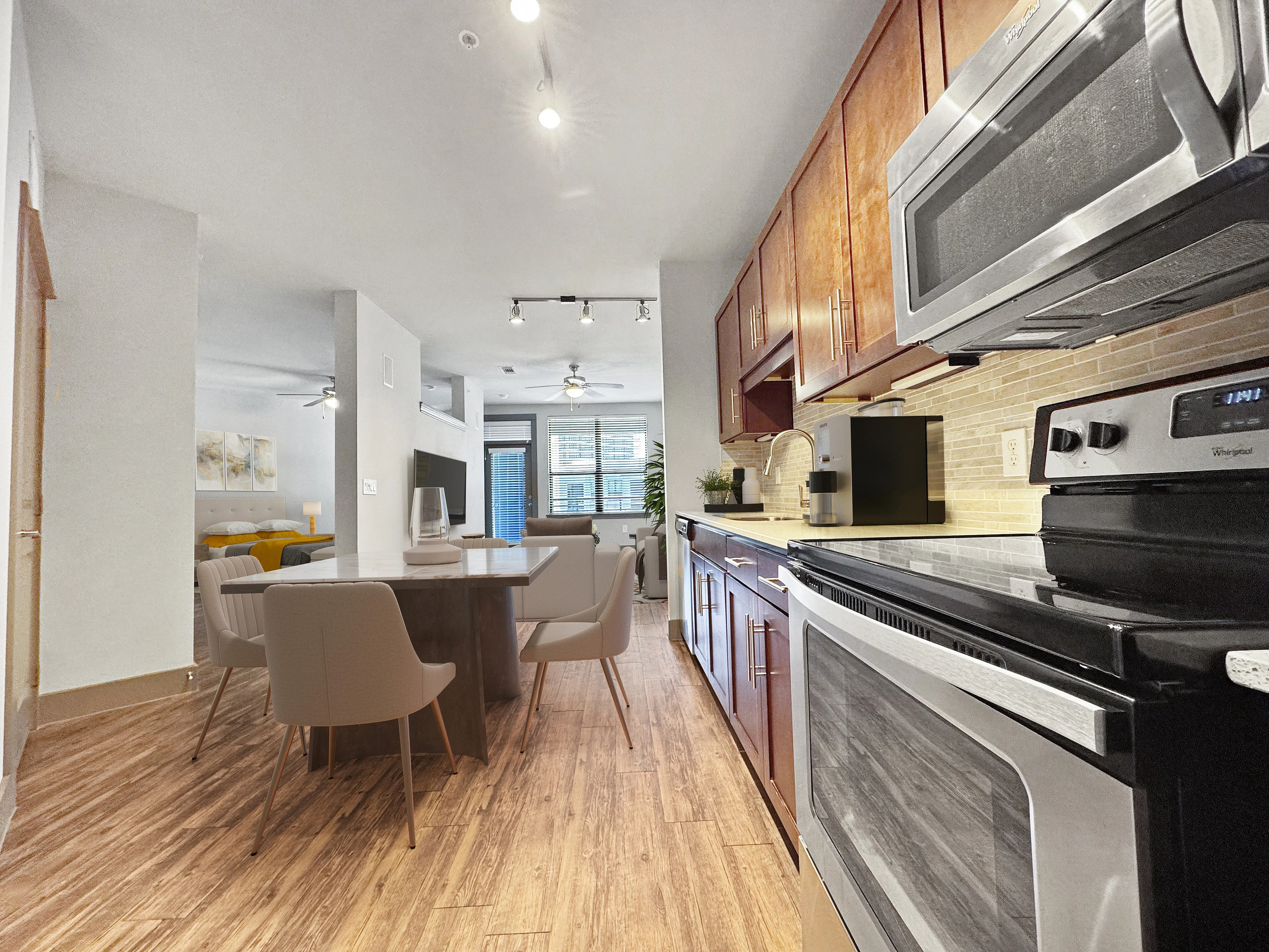Contemporary apartment kitchen with sleek stainless steel appliances, open dining area, and warm wood flooring, leading to a cozy living space filled with natural light.