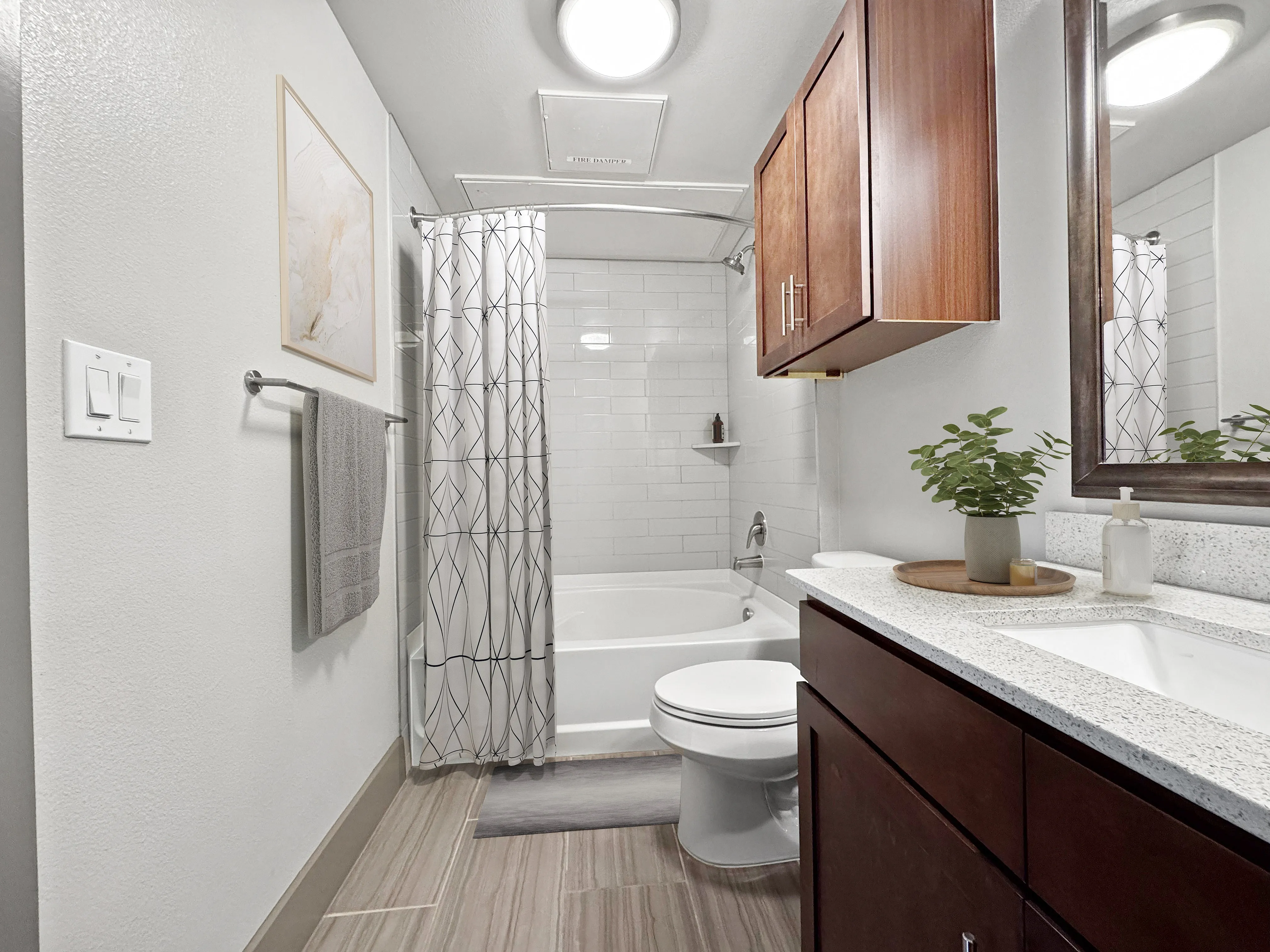 Modern bathroom featuring elegant wooden cabinetry, sleek white tiles, a spacious bathtub, and stylish vanity with greenery.