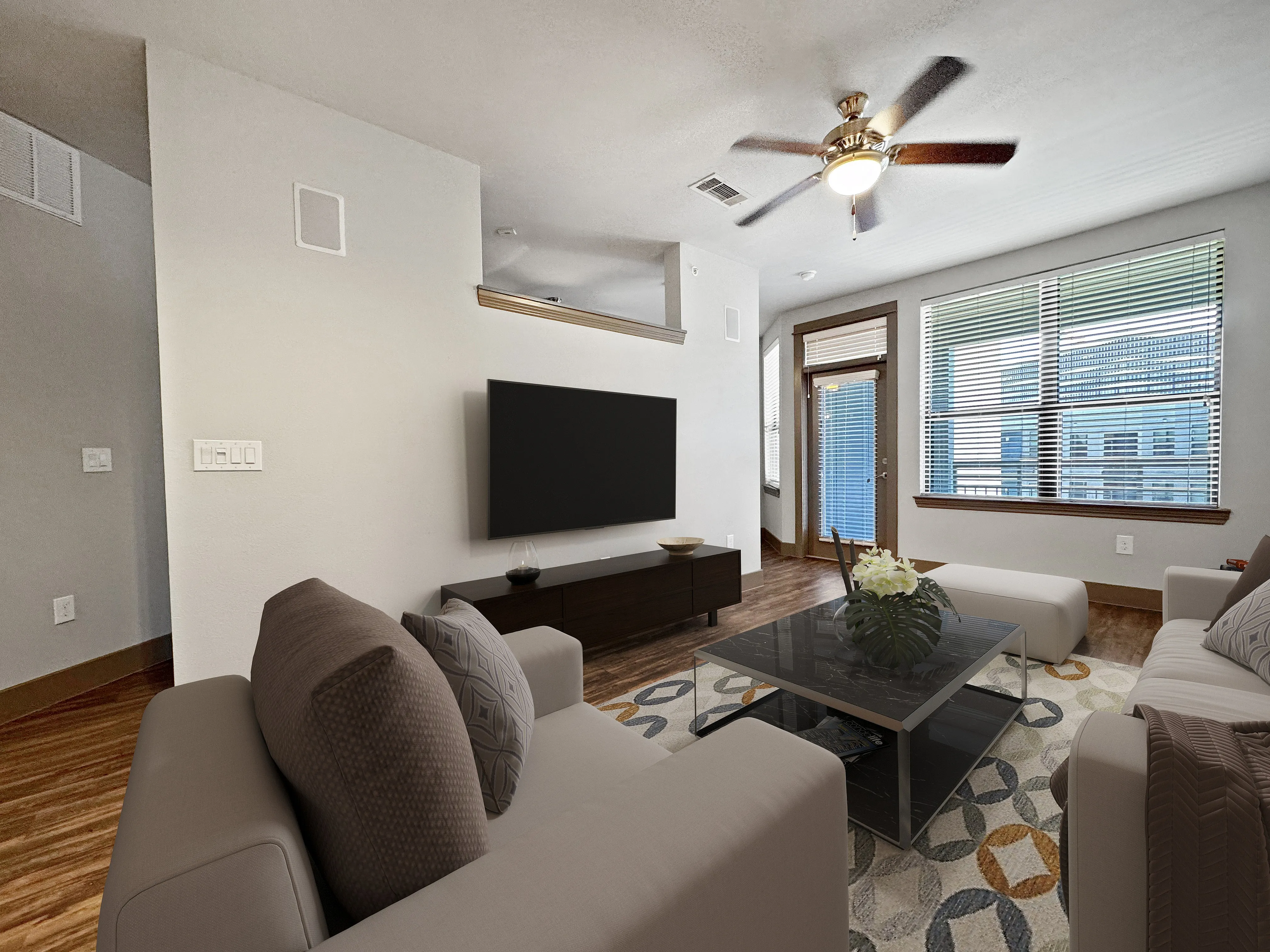 Modern living room with sleek furniture, a stylish ceiling fan, and large windows offering abundant natural light.