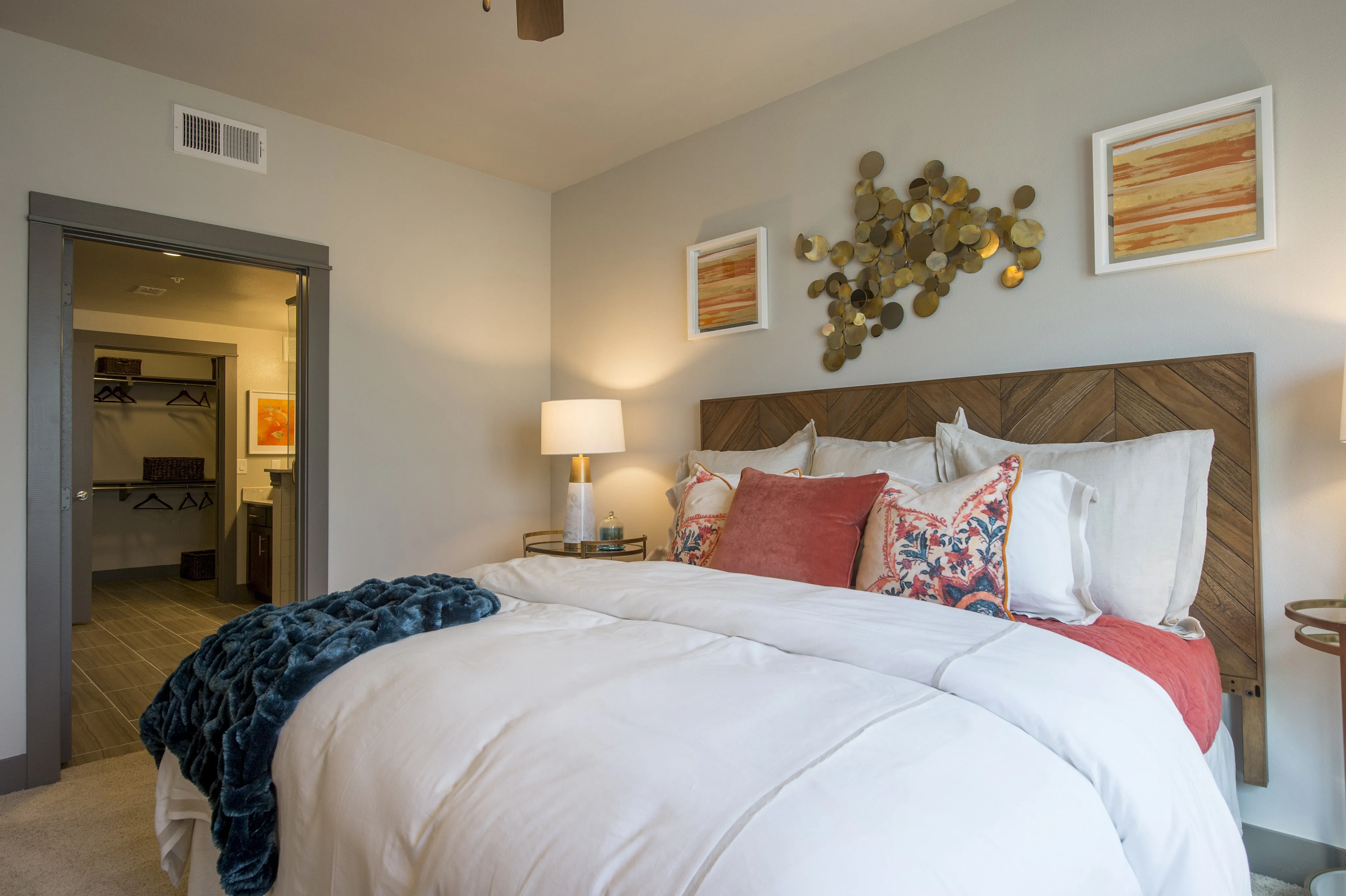 Chic bedroom with elegant wooden headboard, soft white bedding, and vibrant pillows, leading to an organized walk-in closet.