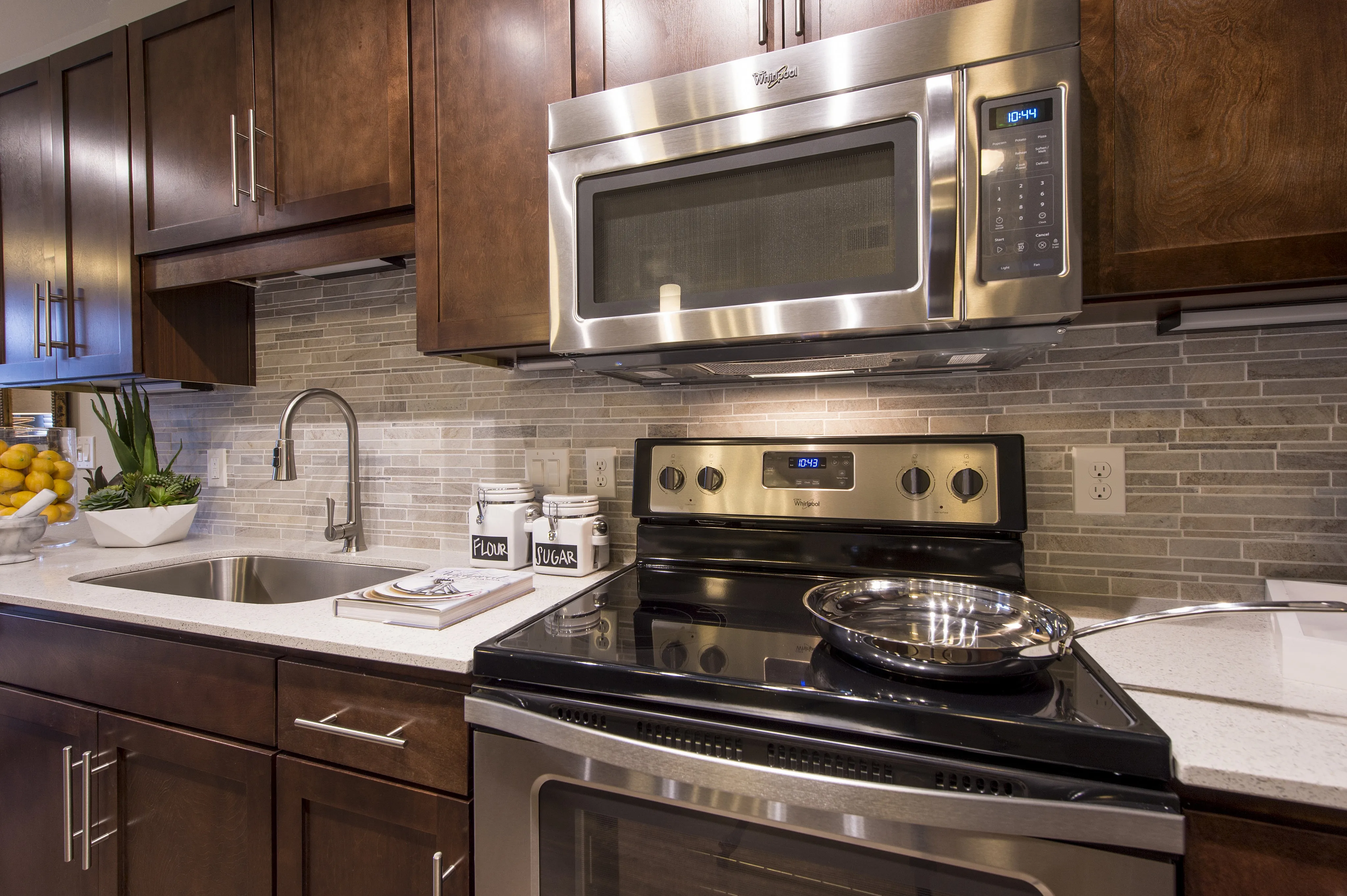Modern kitchen with stainless steel appliances, elegant dark wood cabinetry, and sleek stone backsplash.