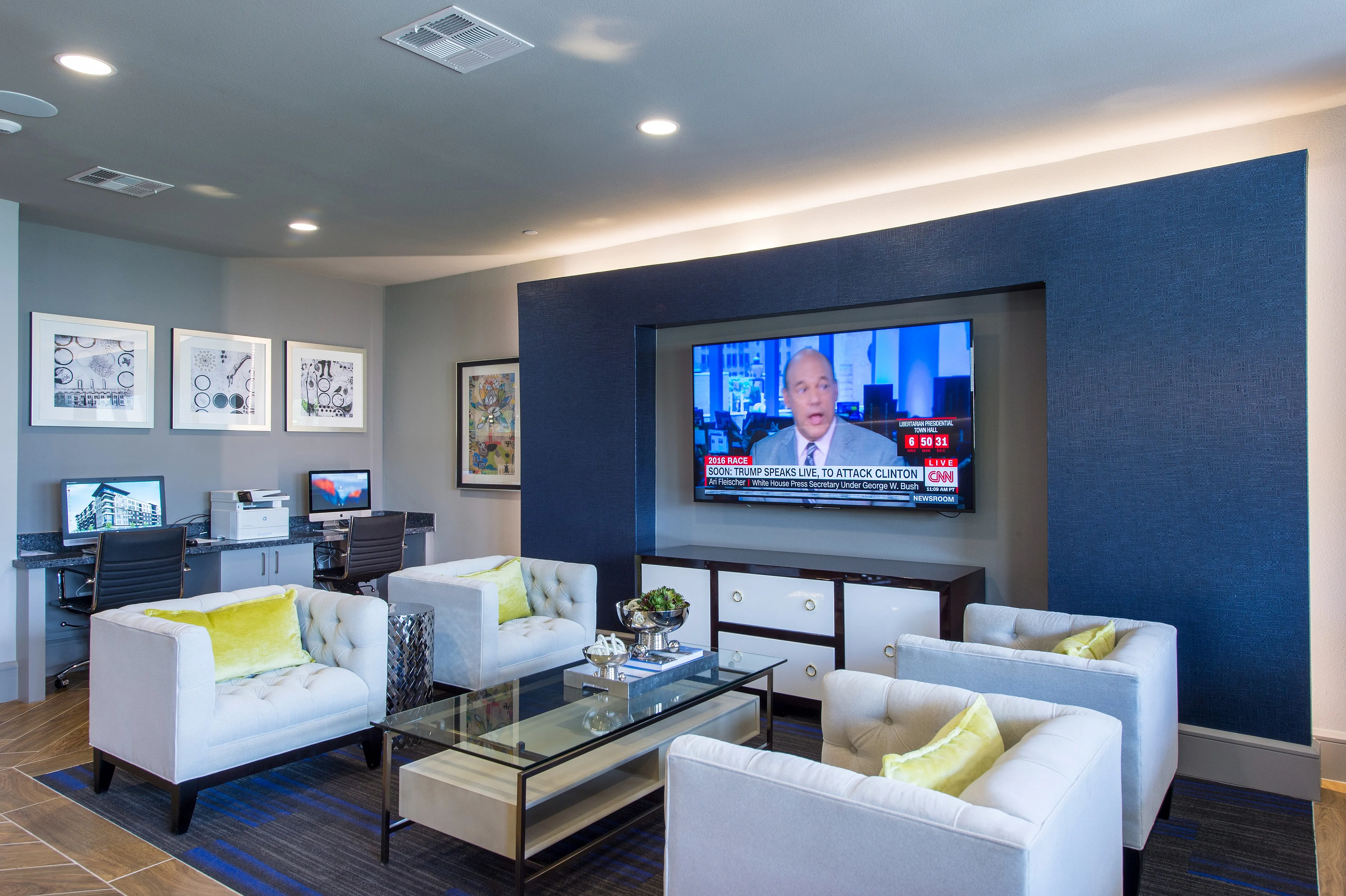 Modern entertainment and workspace area with cozy seating, wall-mounted TV, and computer stations, ideal for relaxation and productivity.