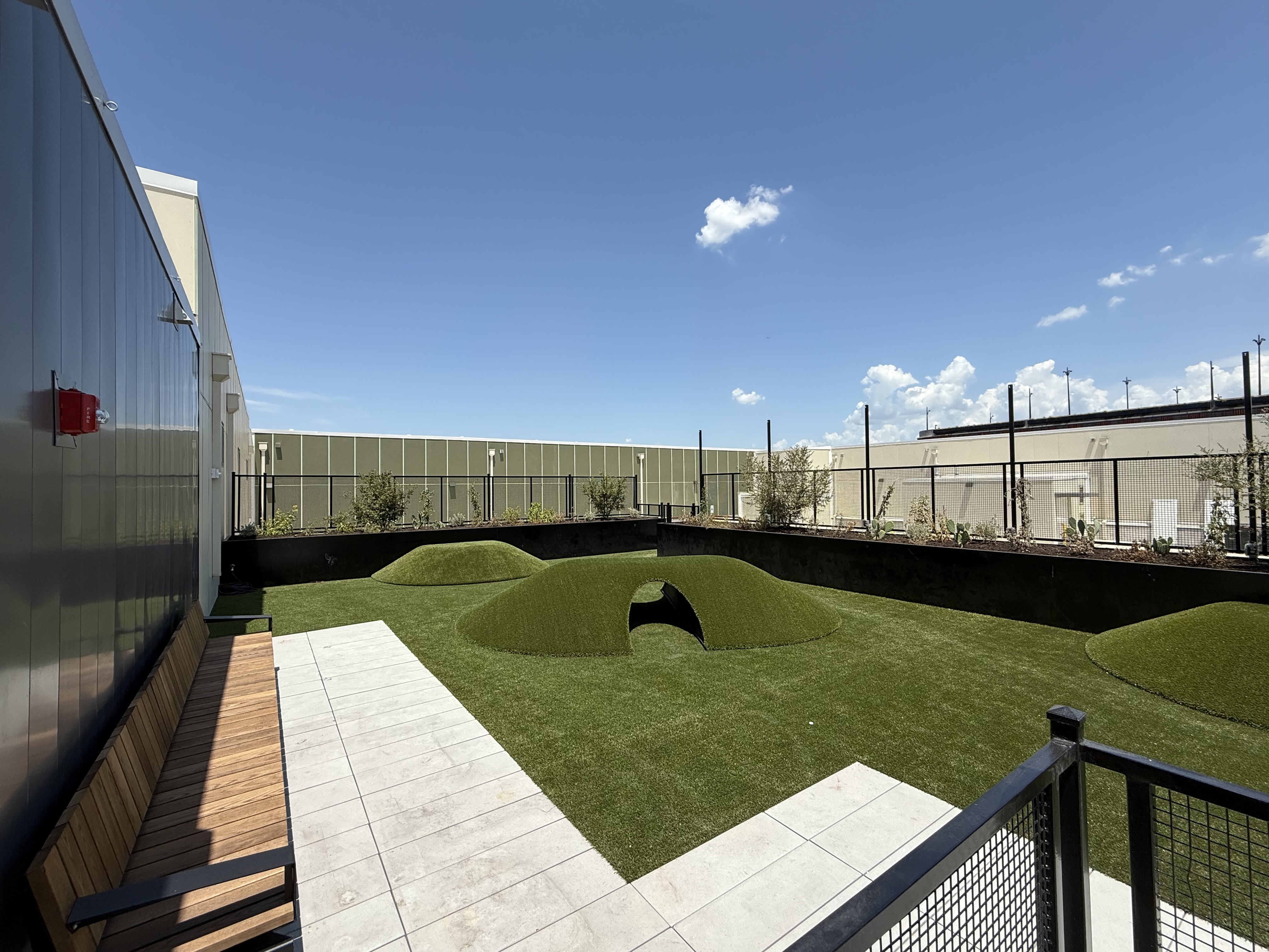 Chic rooftop garden with soft artificial grass mounds, spacious seating, and a panoramic view of clear blue skies.