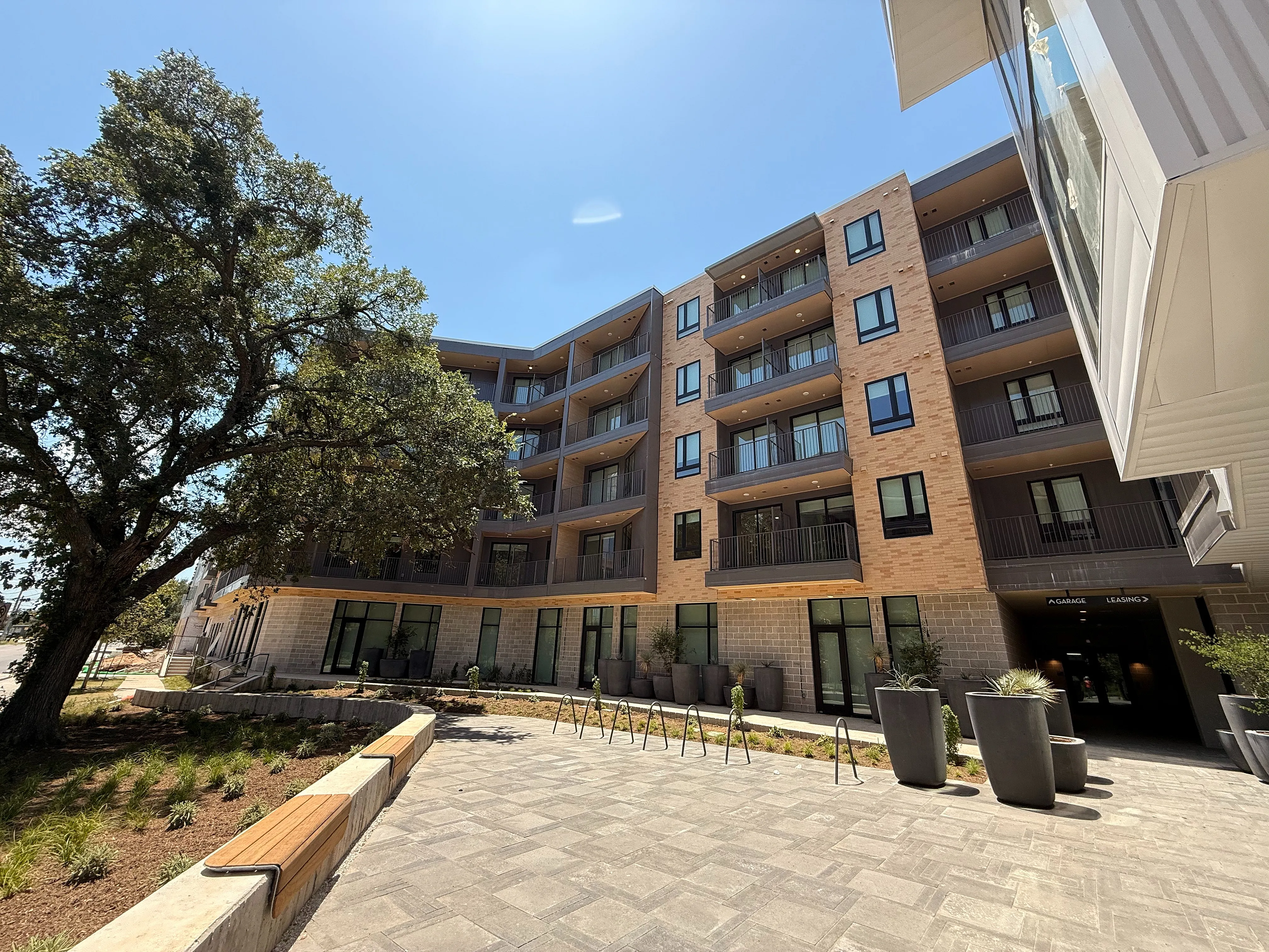 Modern apartment complex exterior with spacious balconies, surrounded by lush landscaping and bright blue sky, perfect for urban living.