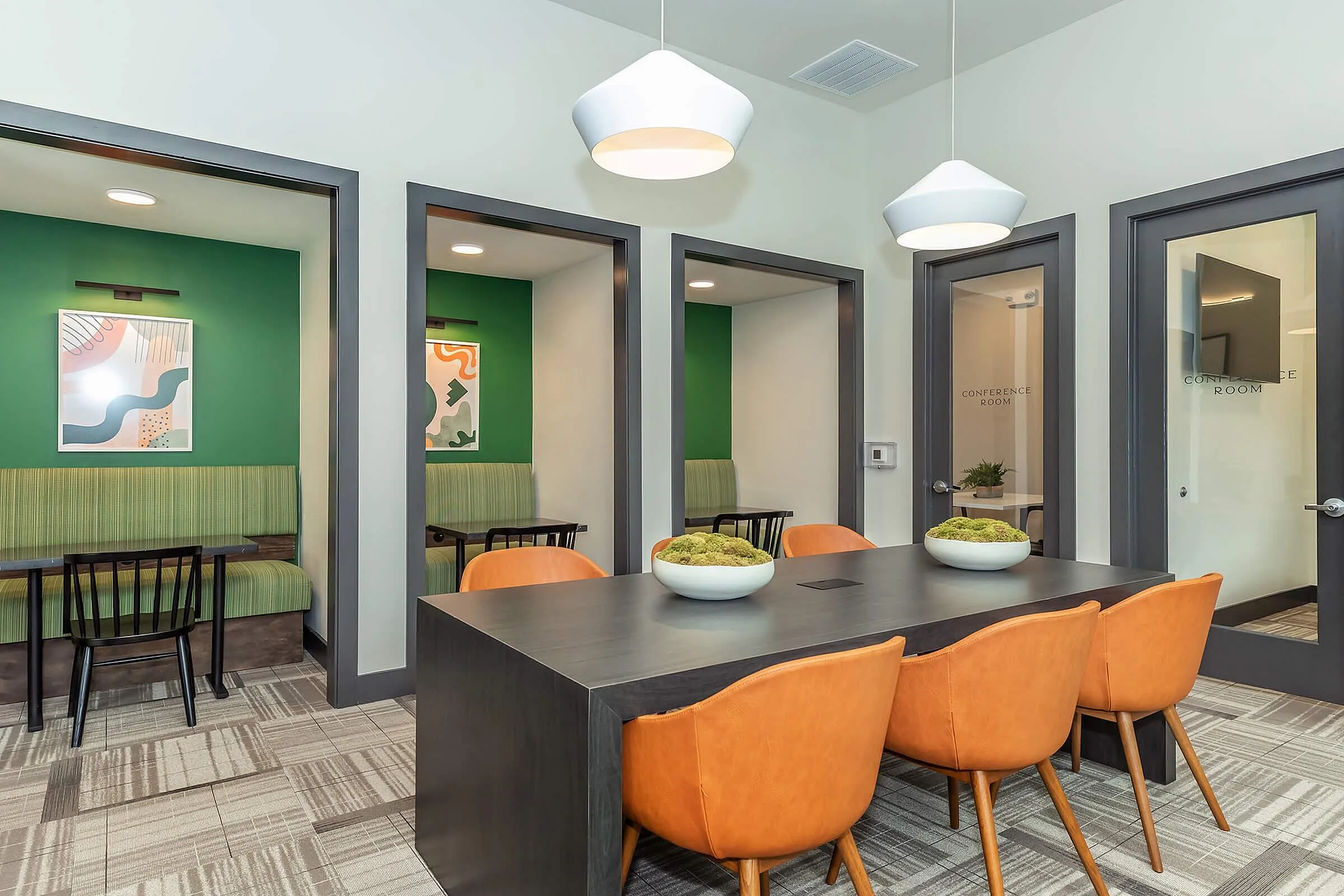 Contemporary meeting space with modern conference table, vibrant orange chairs, and cozy booths in a stylish office setting.