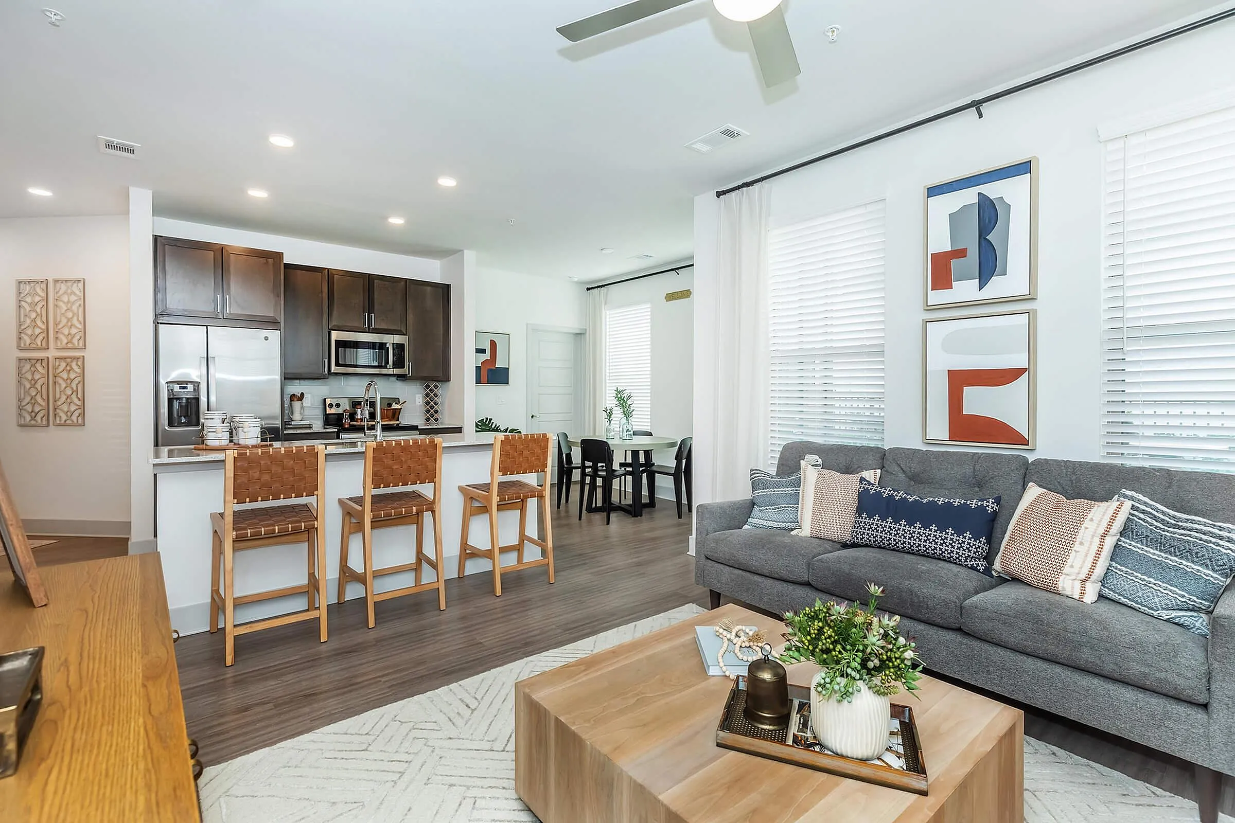 Modern living room showcasing a stylish open-concept kitchen with sleek dark cabinetry and breakfast bar seating; cozy sofa and elegant decor complete the inviting space.