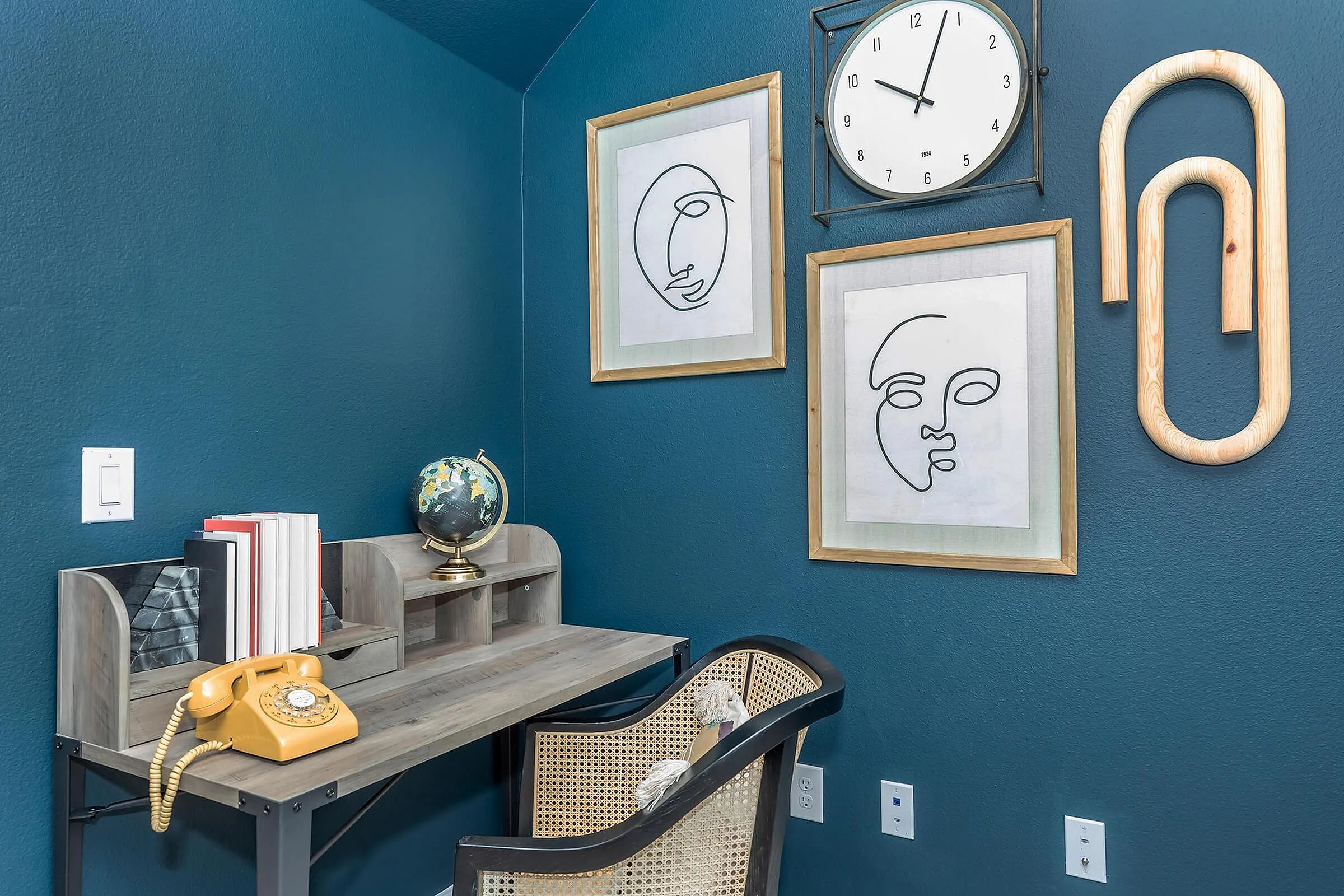 Charming home office with teal walls, vintage rotary phone, sleek wooden desk, and modern art accents for a cozy work environment.