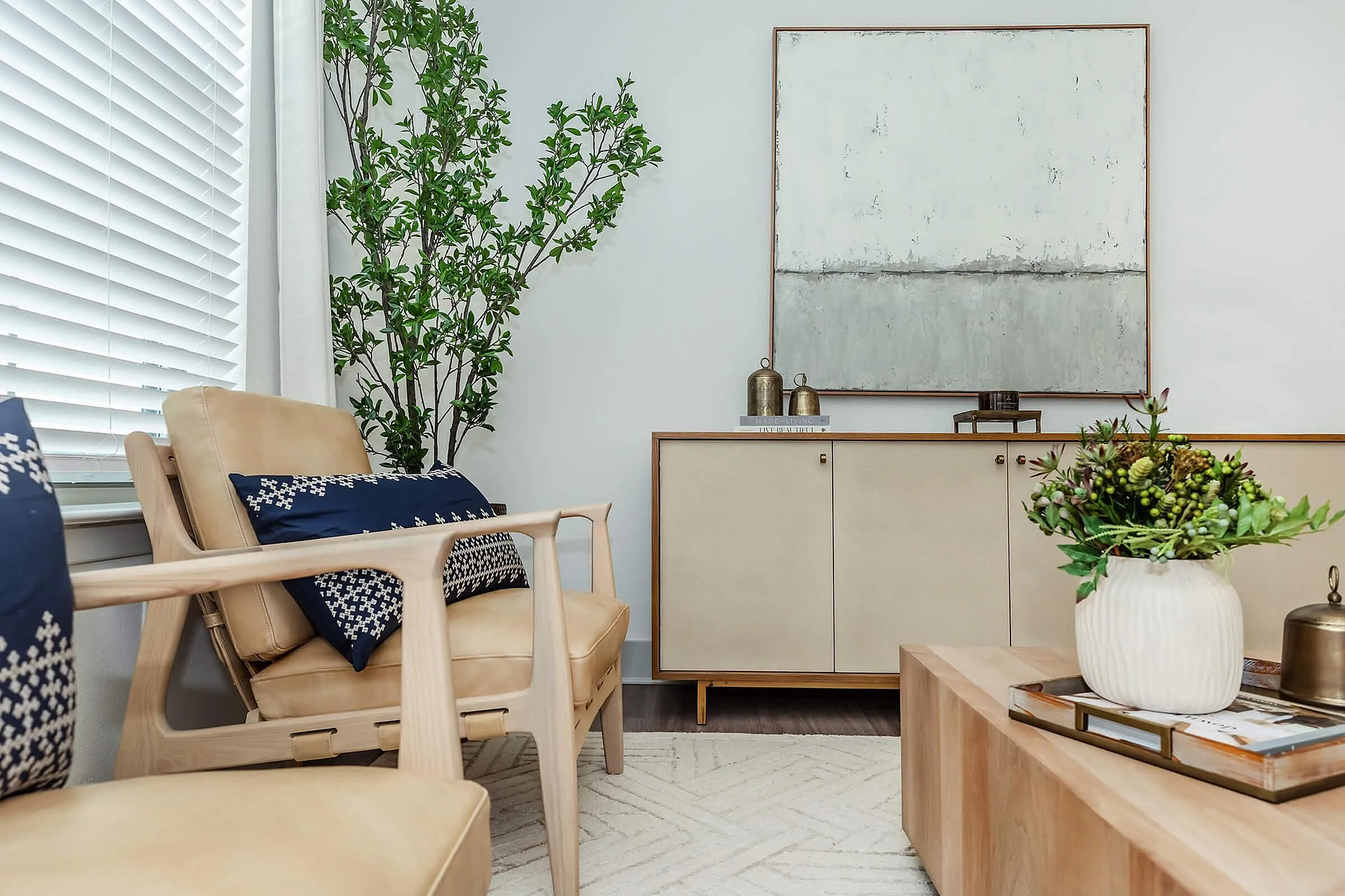 Inviting modern living room with elegant decor, featuring a chic abstract painting, lush green plant, and stylish beige furniture accented by navy pillows.