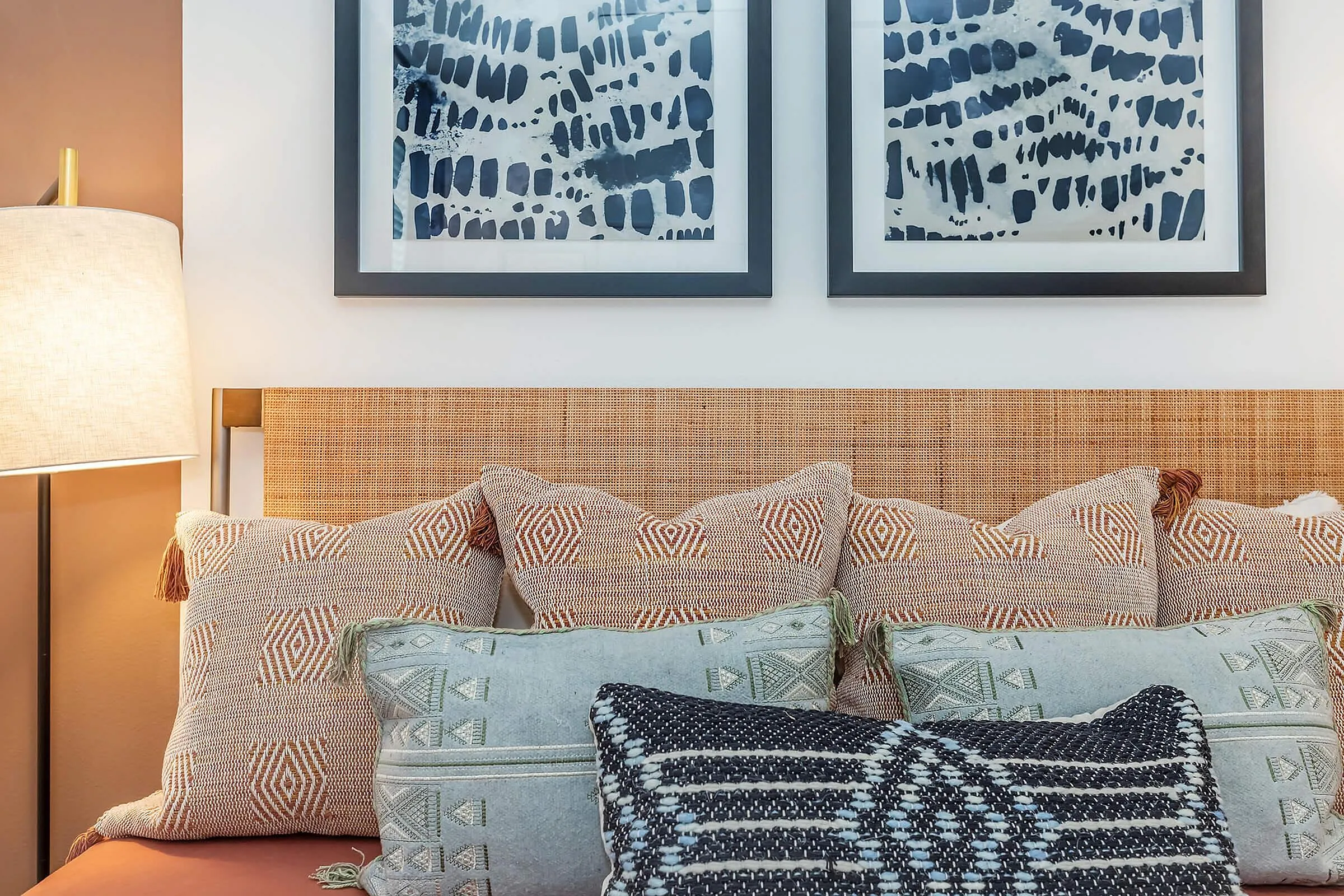 Cozy bedroom setting featuring a wicker headboard with elegant patterned pillows and abstract wall art in a warm, inviting ambiance.