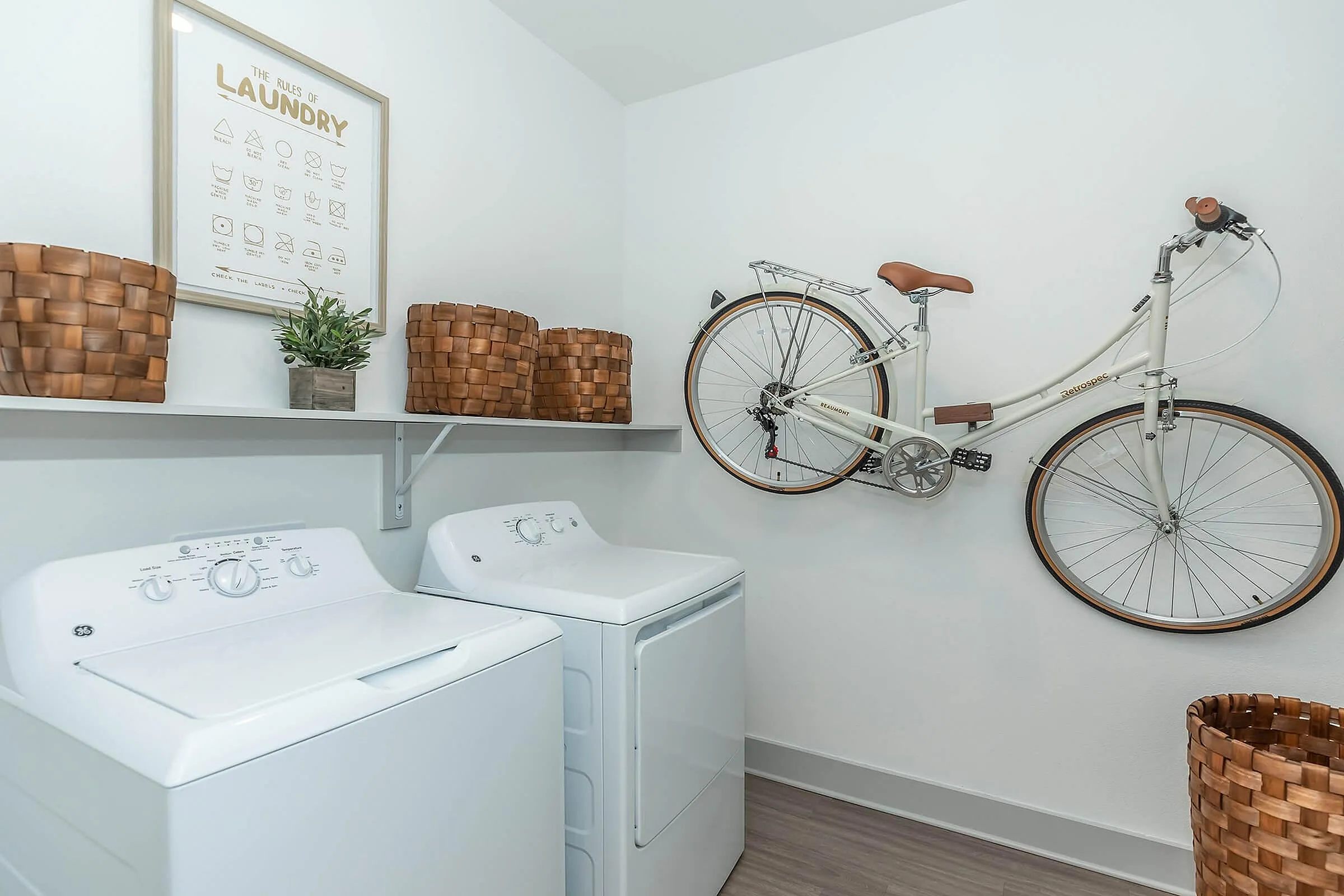 Modern laundry room with washing machine, dryer, stylish woven baskets, and a mounted vintage bicycle for chic storage.
