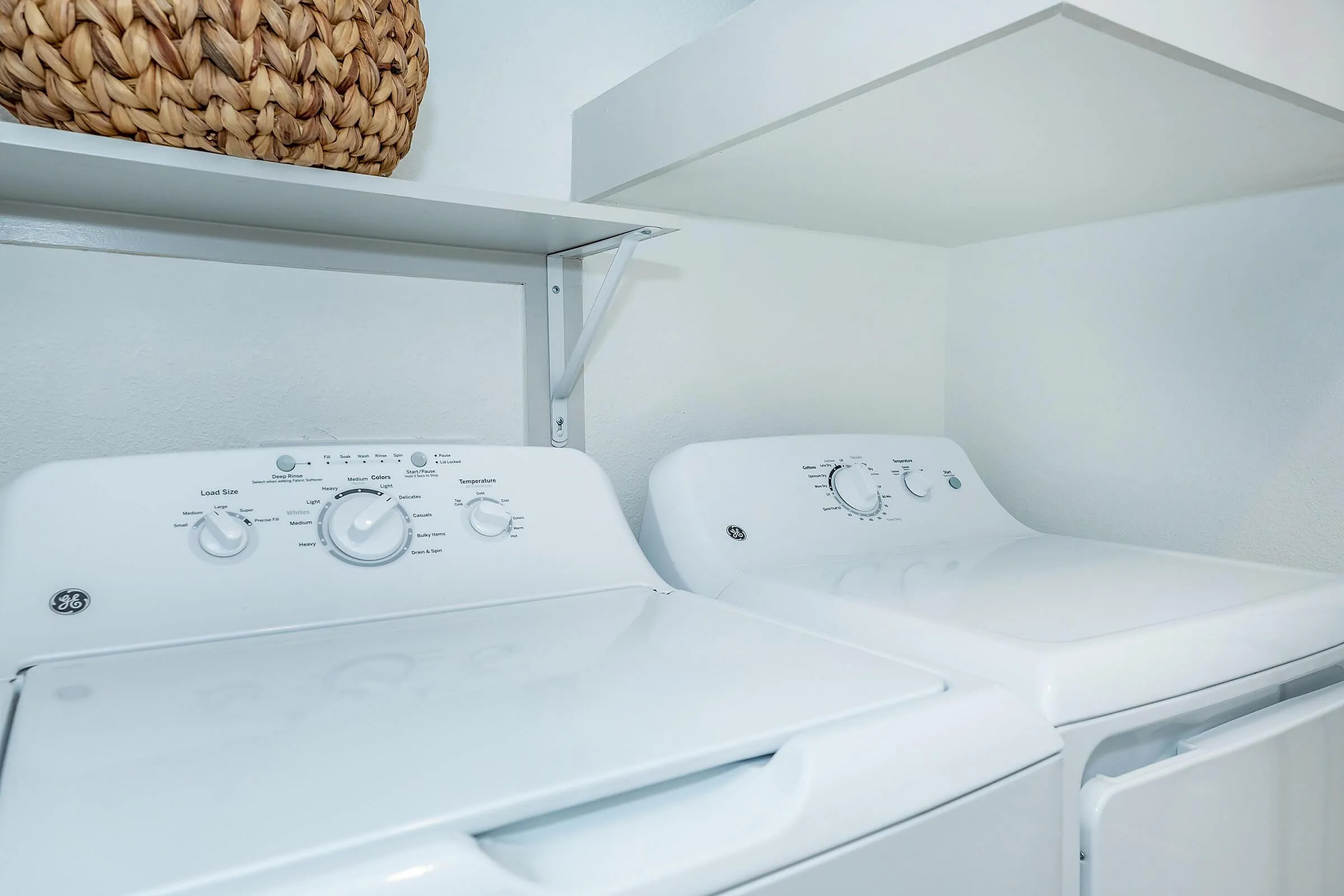 Modern laundry area with sleek white washer and dryer, accentuated by a chic woven basket on a stylish shelf.