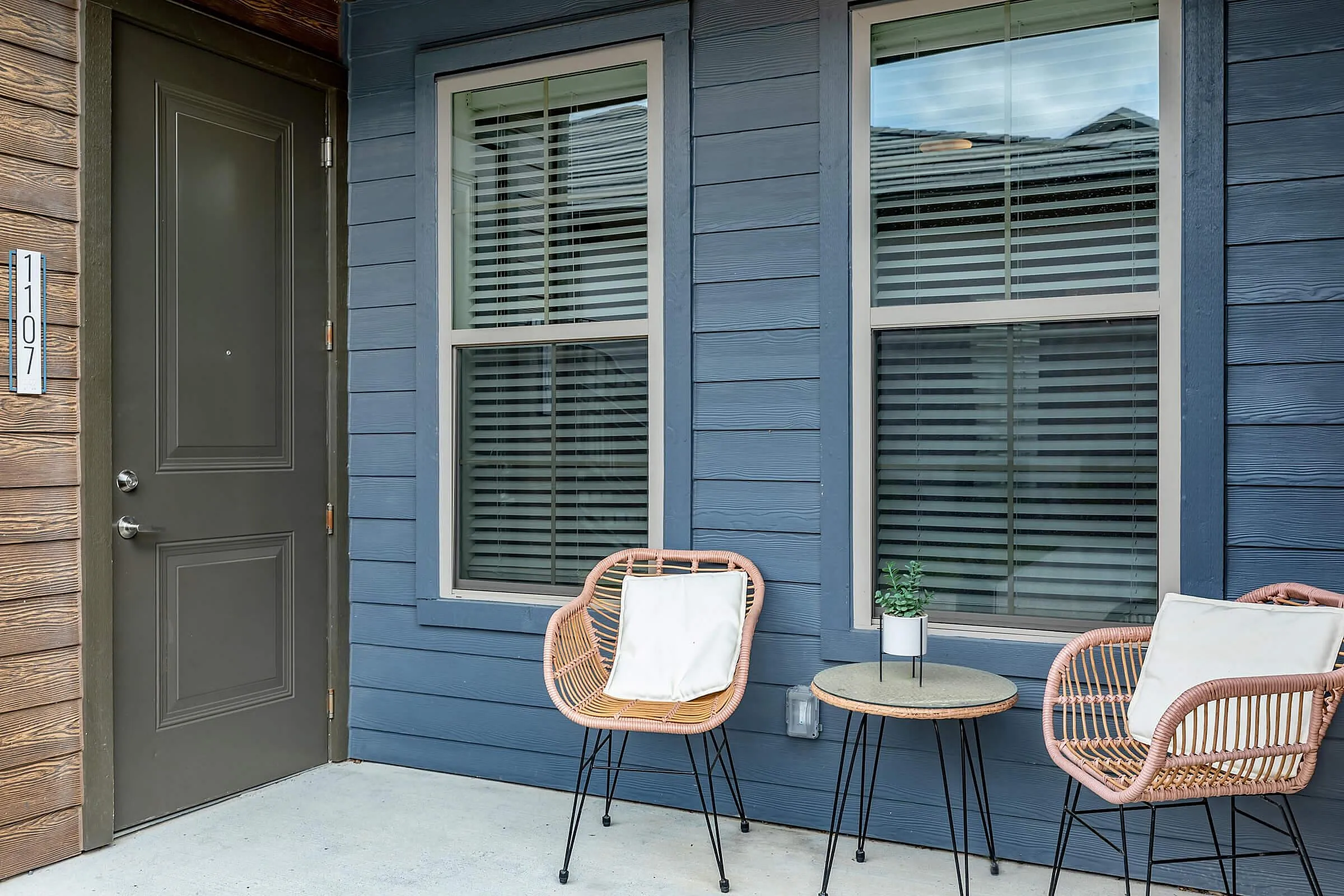 Inviting apartment entryway with stylish outdoor seating and modern blue siding, perfect for relaxation.