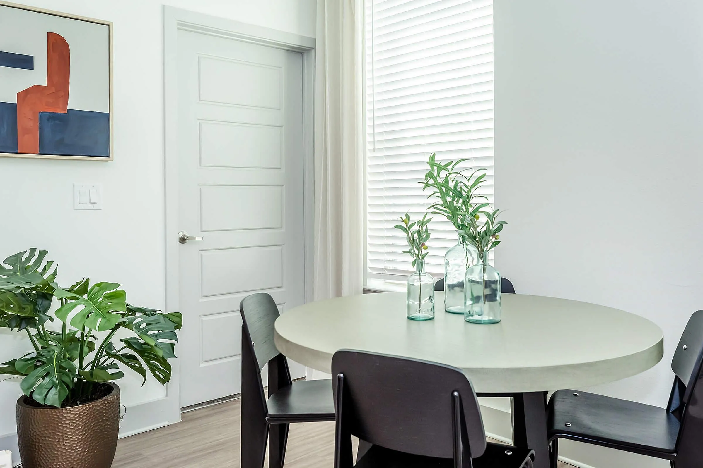 Contemporary dining area with sleek round table, modern chairs, and stylish decor featuring vibrant artwork and greenery.