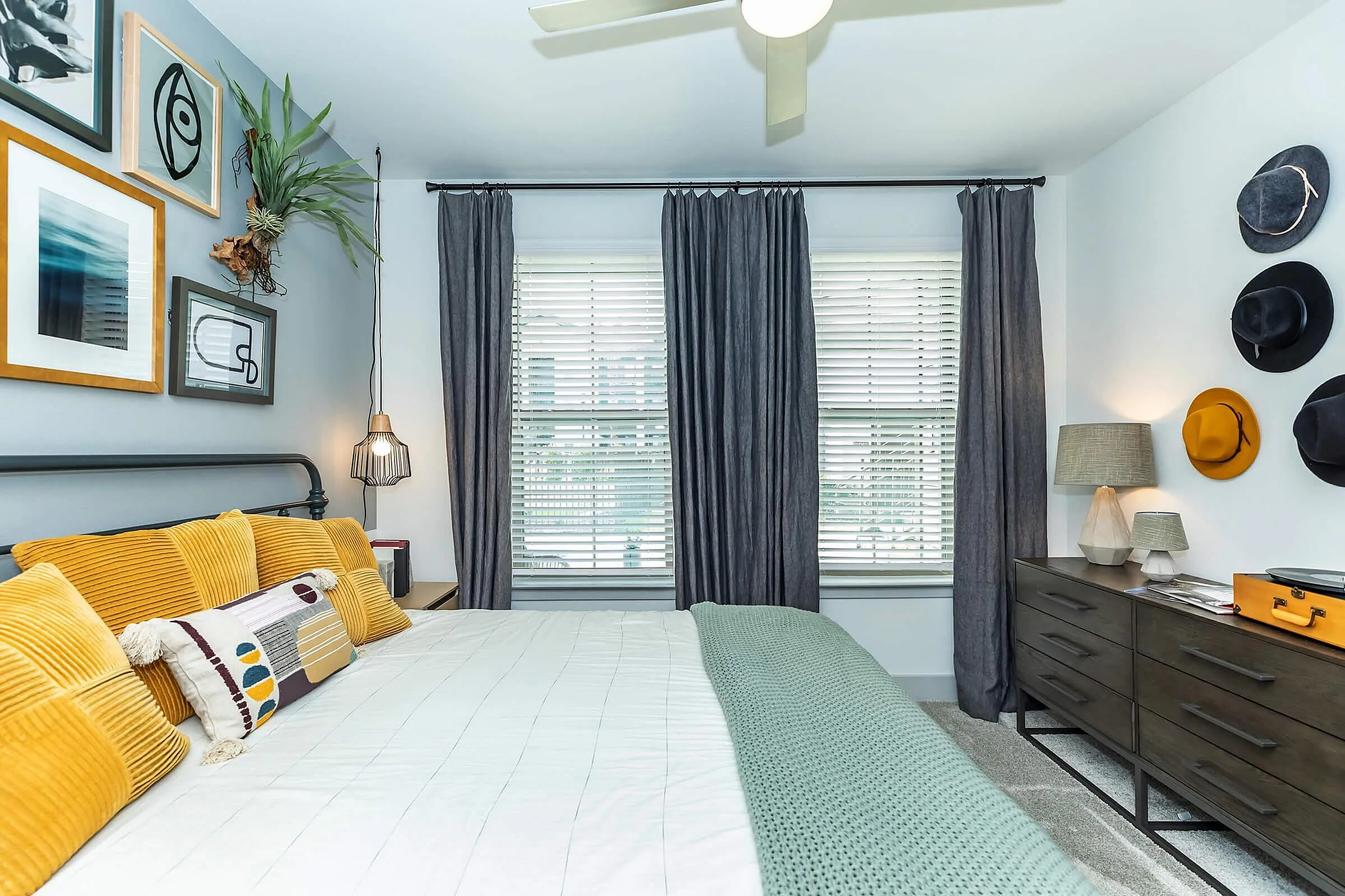 Chic bedroom with modern decor, featuring a comfortable bed with mustard pillows, stylish wall art, and a sleek dresser under natural light.