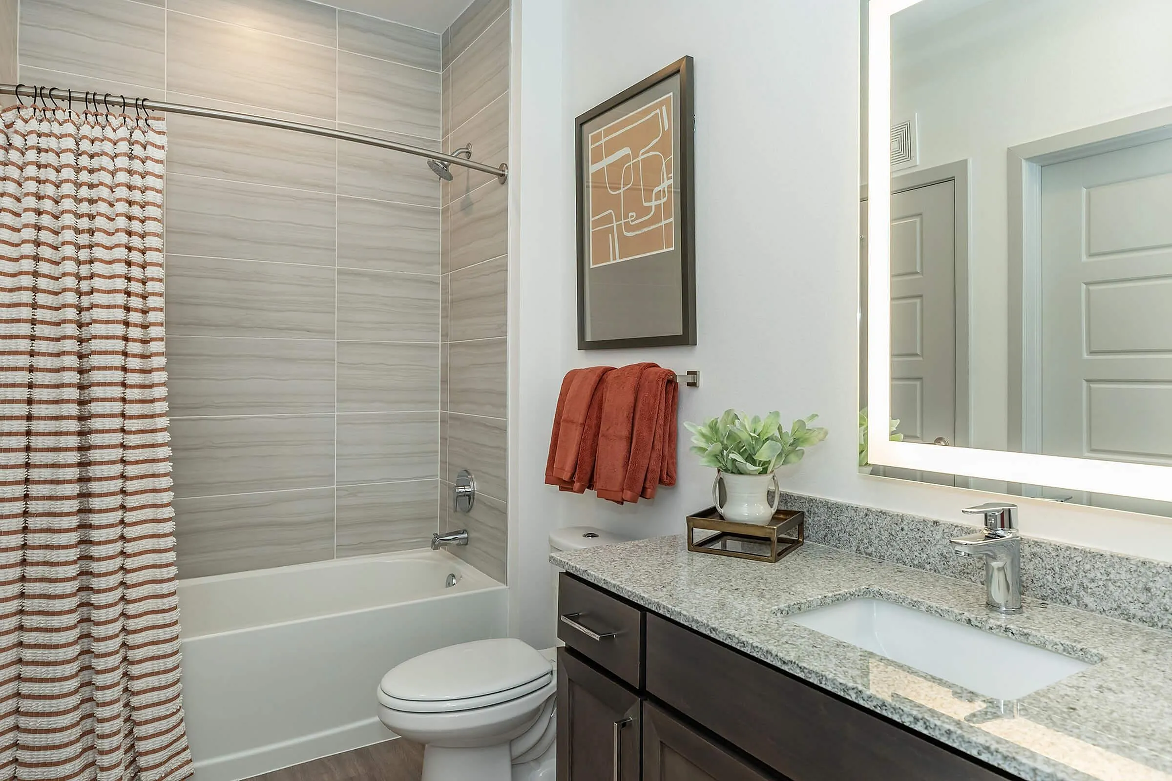 Modern bathroom featuring a stylish granite vanity, illuminated mirror, and elegant tiled shower with a chic curtain.