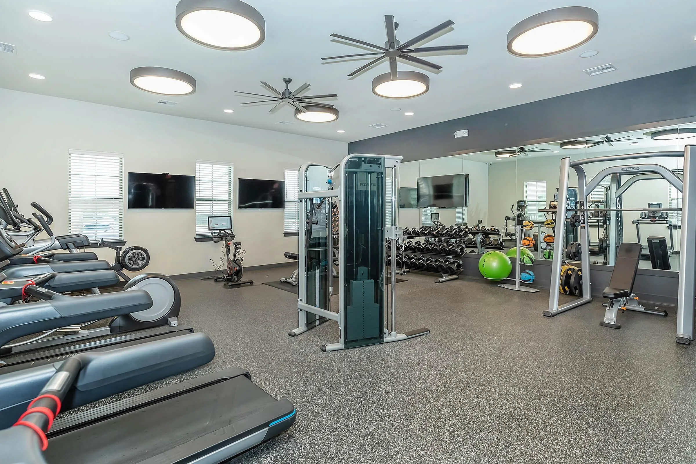 Modern fitness center with state-of-the-art gym equipment, featuring treadmills, exercise bikes, weight machines, and free weights in a spacious, well-lit room.