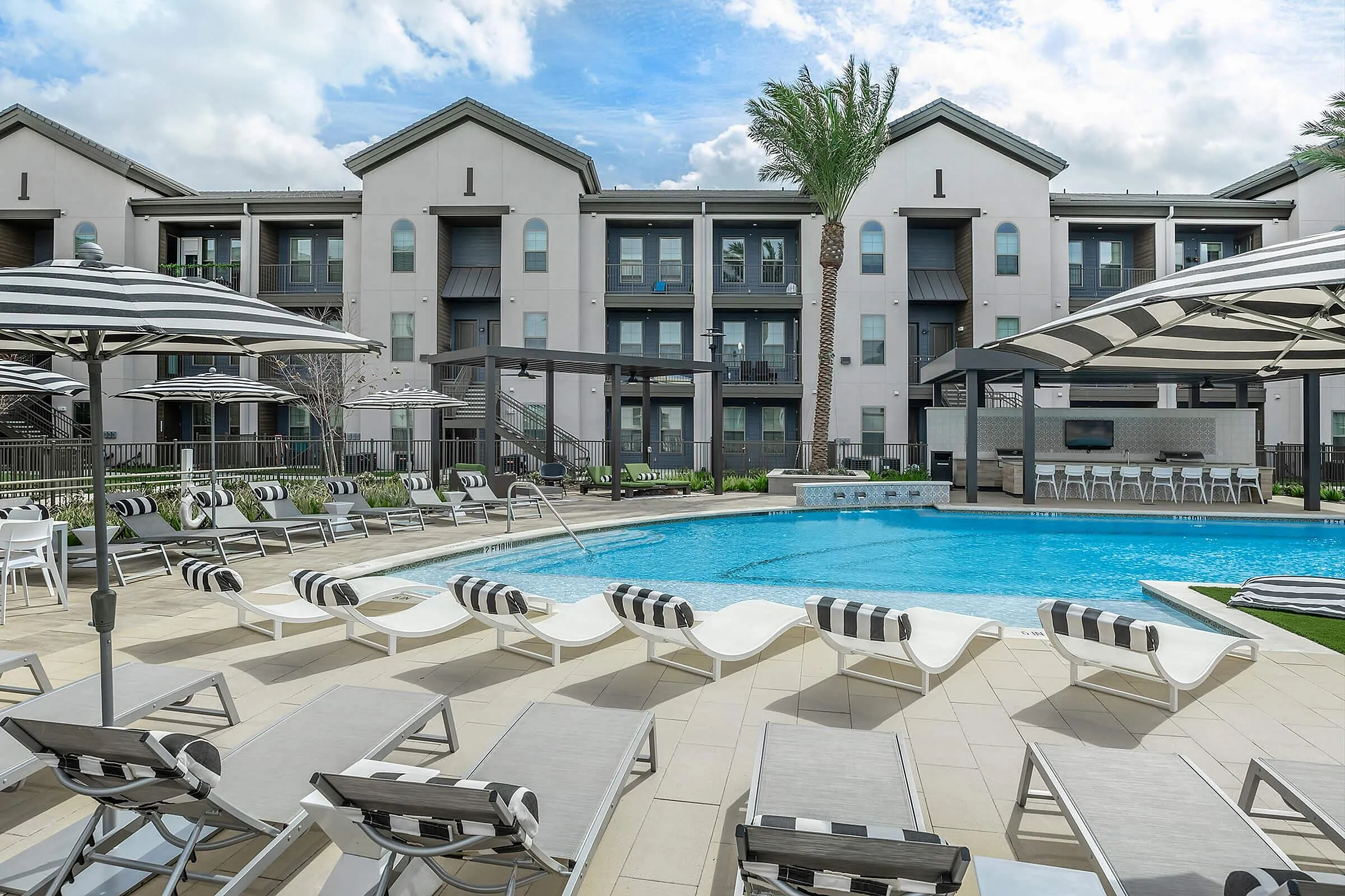 Luxurious apartment complex featuring a shimmering outdoor pool, stylish lounge chairs, and modern architecture, perfect for relaxing and unwinding.