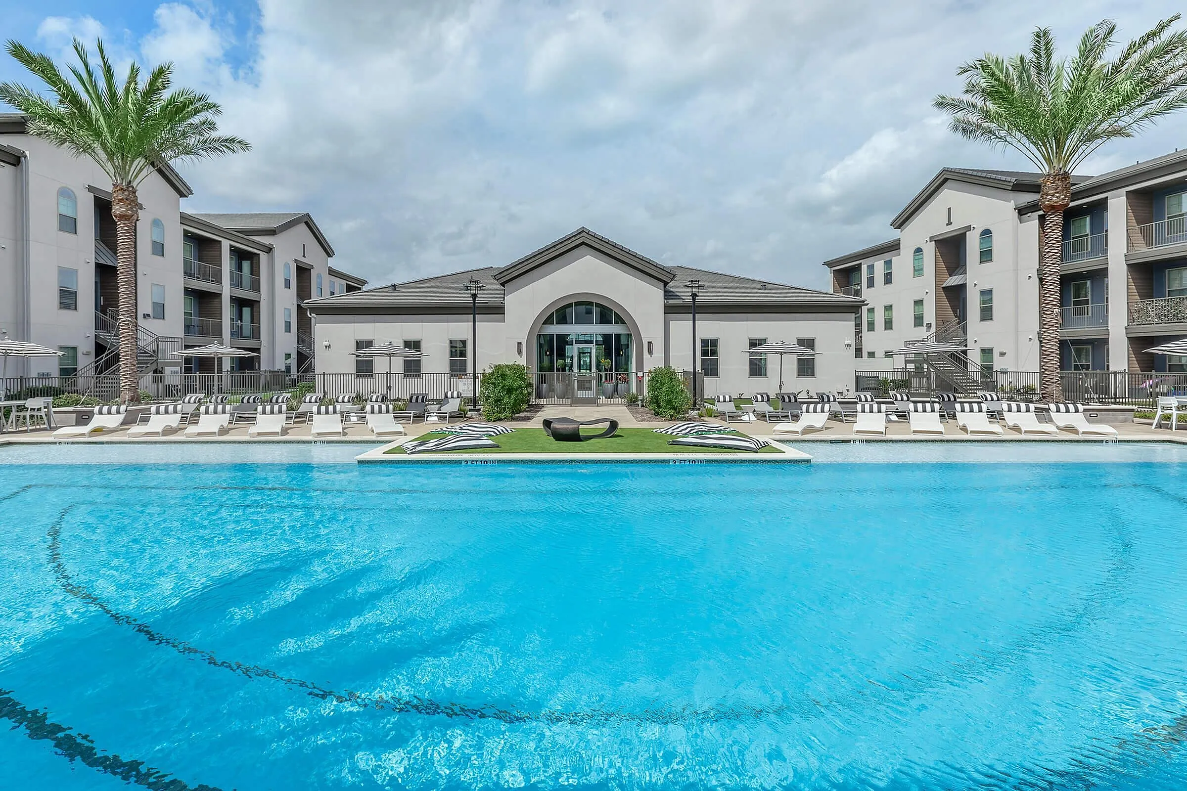 Luxurious apartment complex featuring a sparkling blue pool, surrounded by stylish lounge chairs and elegant palm trees, perfect for relaxation and leisure.