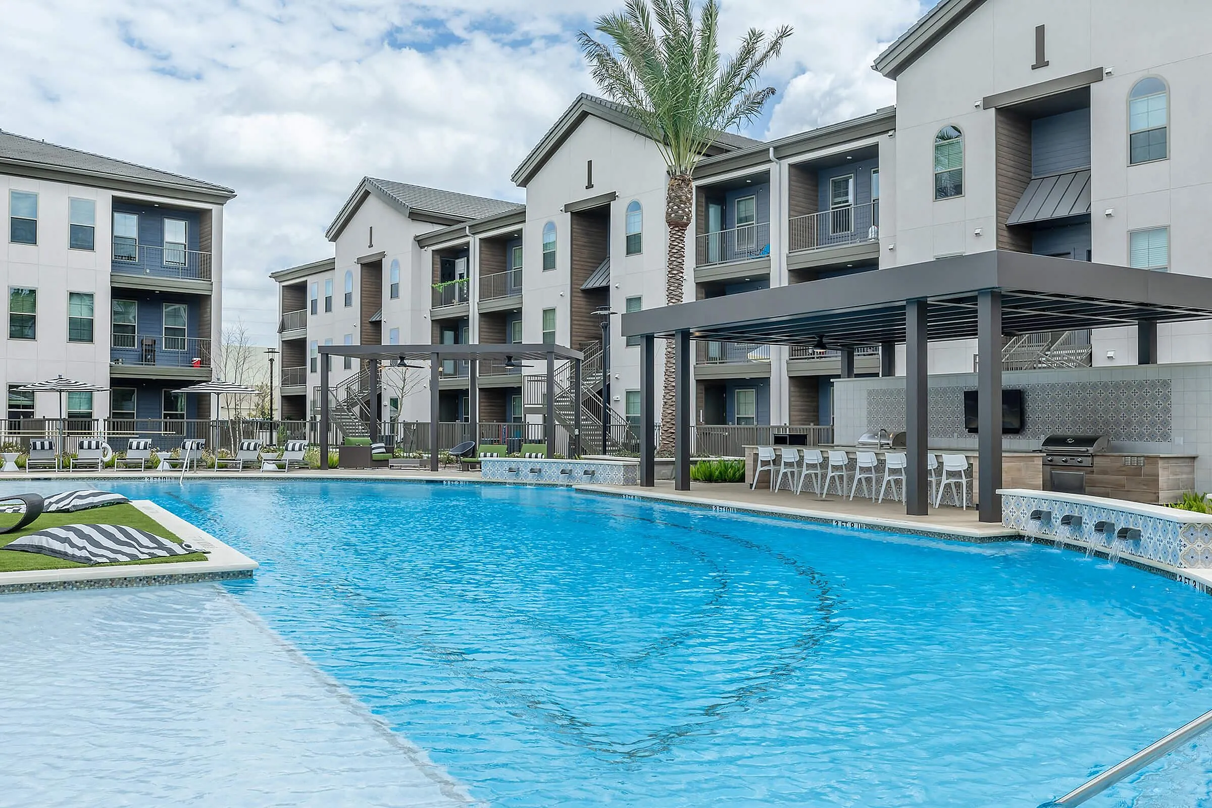 Luxurious apartment complex with modern architecture featuring a sparkling swimming pool, elegant poolside lounging area, and stylish outdoor seating under a shaded pergola.