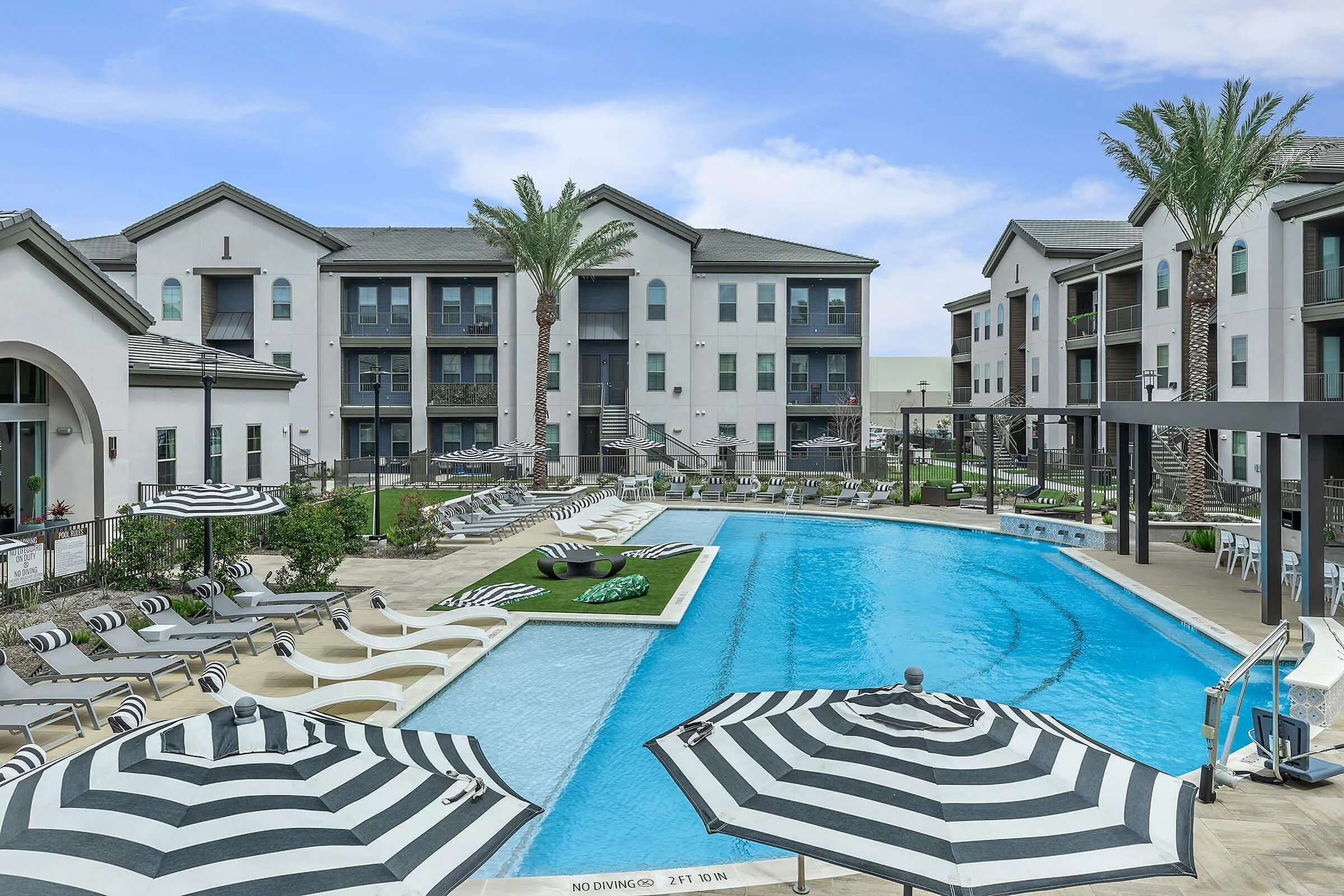 Luxurious apartment complex showcasing a pristine swimming pool surrounded by elegant lounge chairs and stylish black-and-white umbrellas, offering a resort-style living experience.