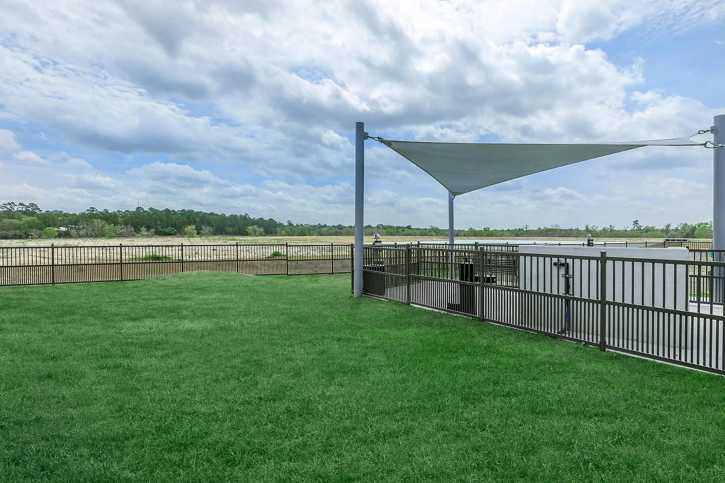 Expansive green lawn with modern fencing and shade sail, offering stunning scenic views of a vast open field under a partly cloudy sky.