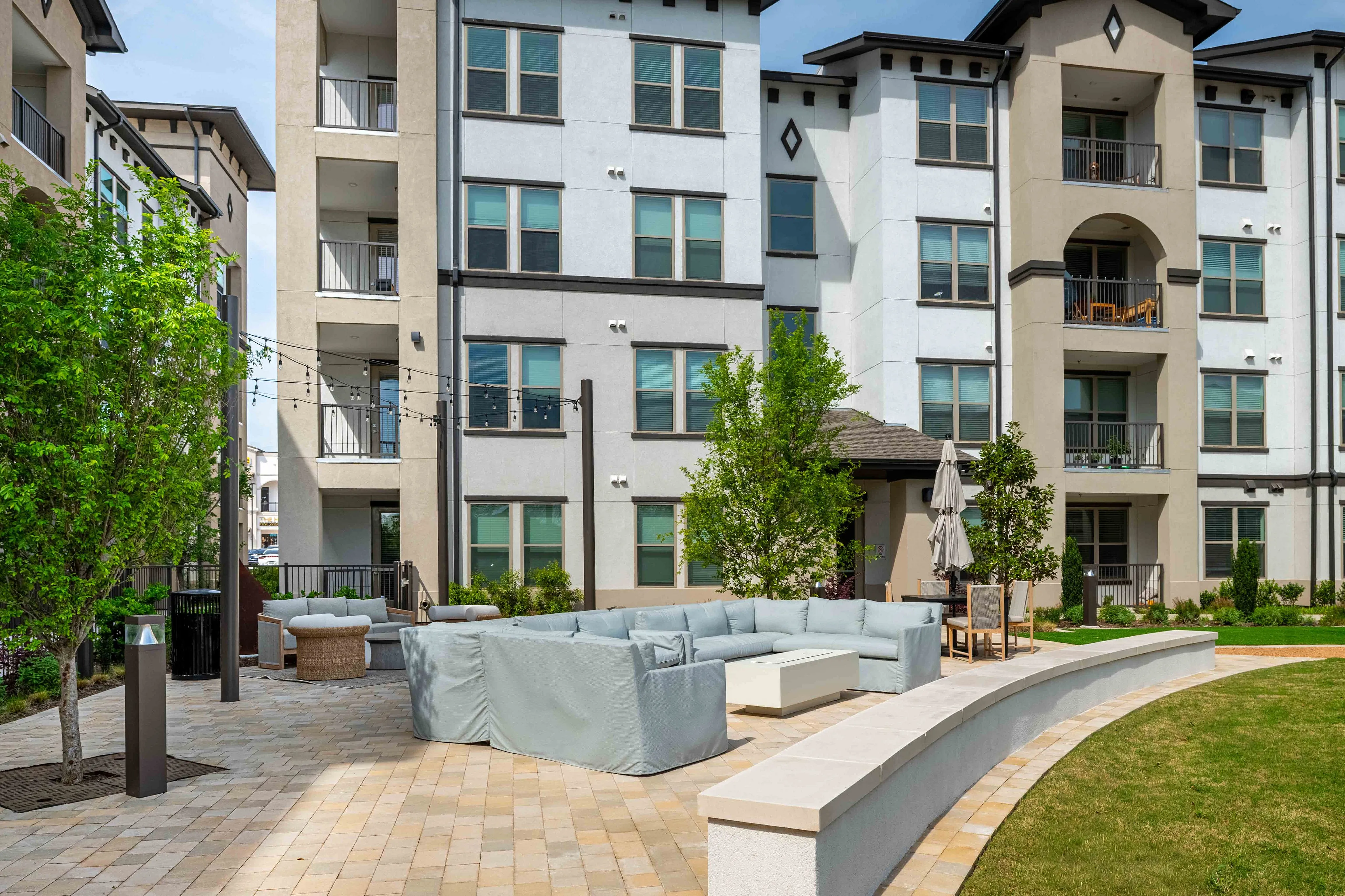 Contemporary apartment complex featuring stylish outdoor seating area with cozy couches and lush greenery.
