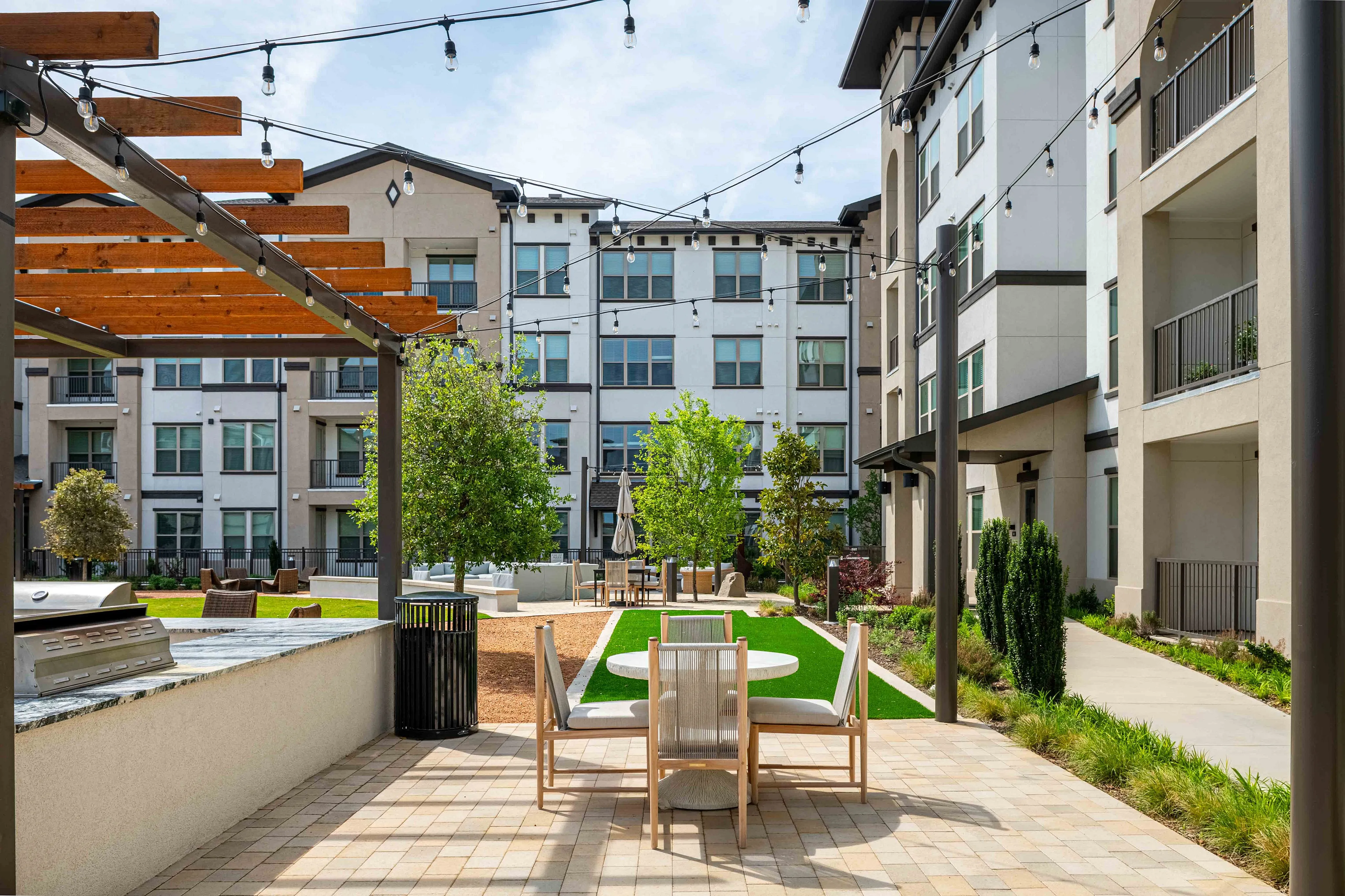 Modern apartment courtyard with elegant outdoor seating, vibrant greenery, and warm string lighting for a welcoming ambiance.