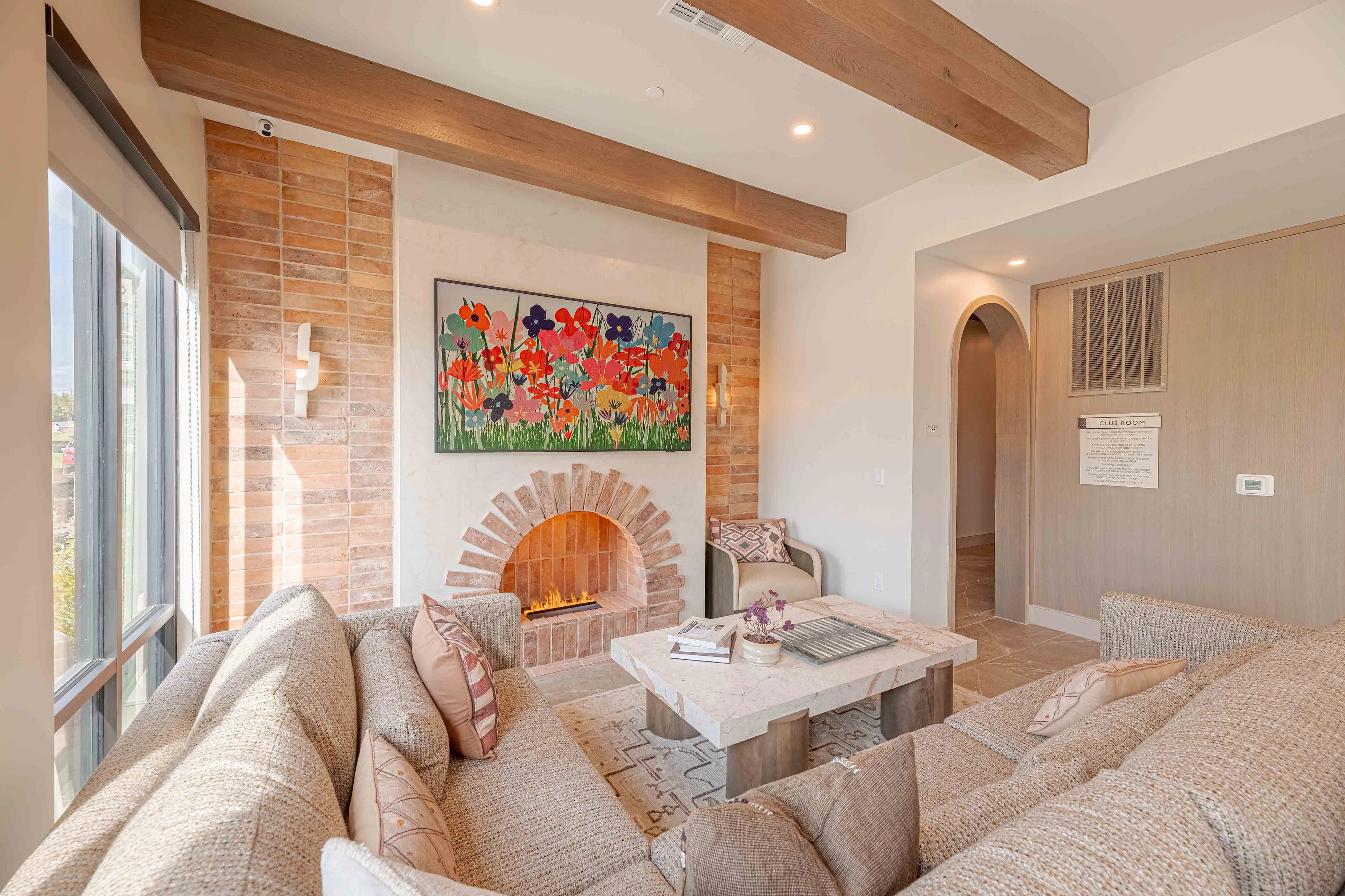 Inviting living room with cozy beige sofas, vibrant floral artwork, and a charming arch-brick fireplace.