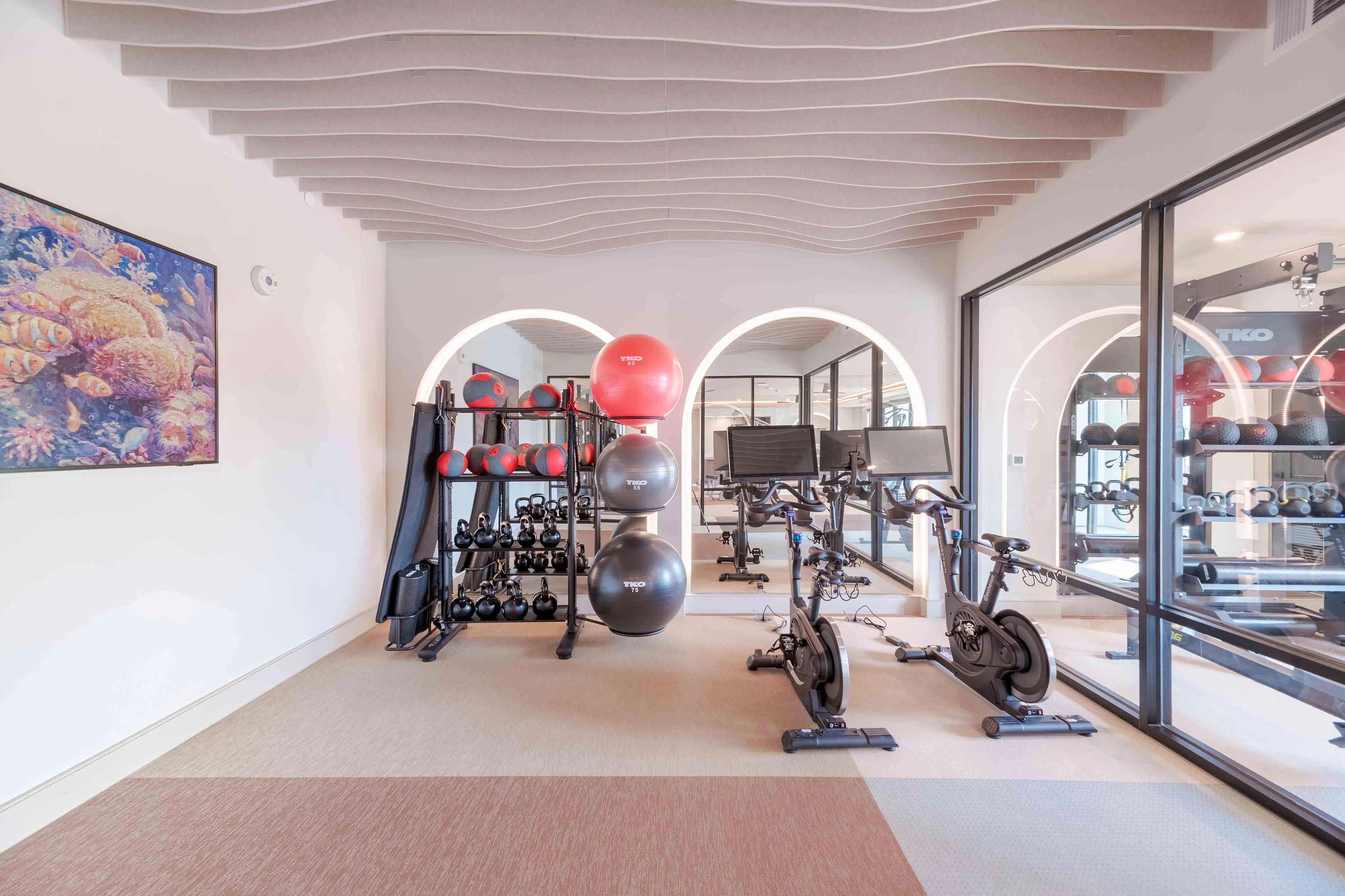Modern fitness room featuring sleek exercise bikes, stylish equipment, and beautifully designed wavy ceiling panels.