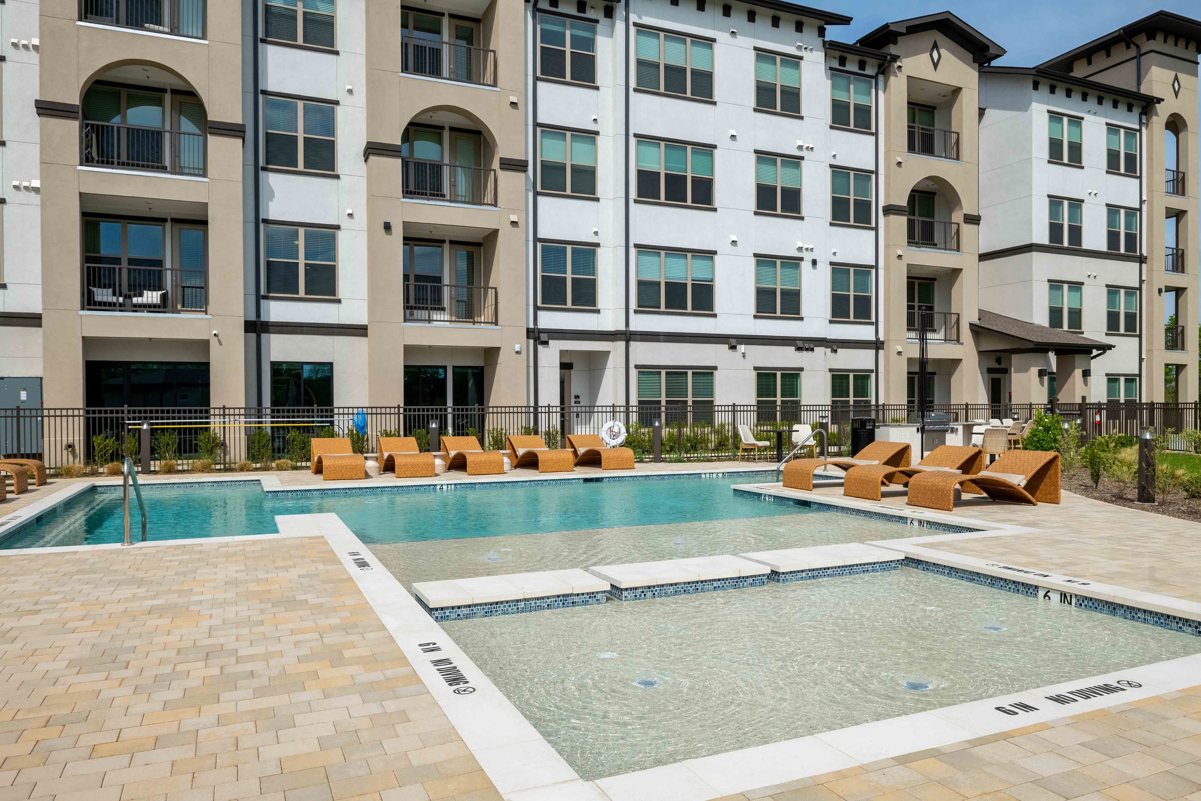 Modern apartment complex featuring a luxurious pool area with stylish lounge seating and a spacious patio.