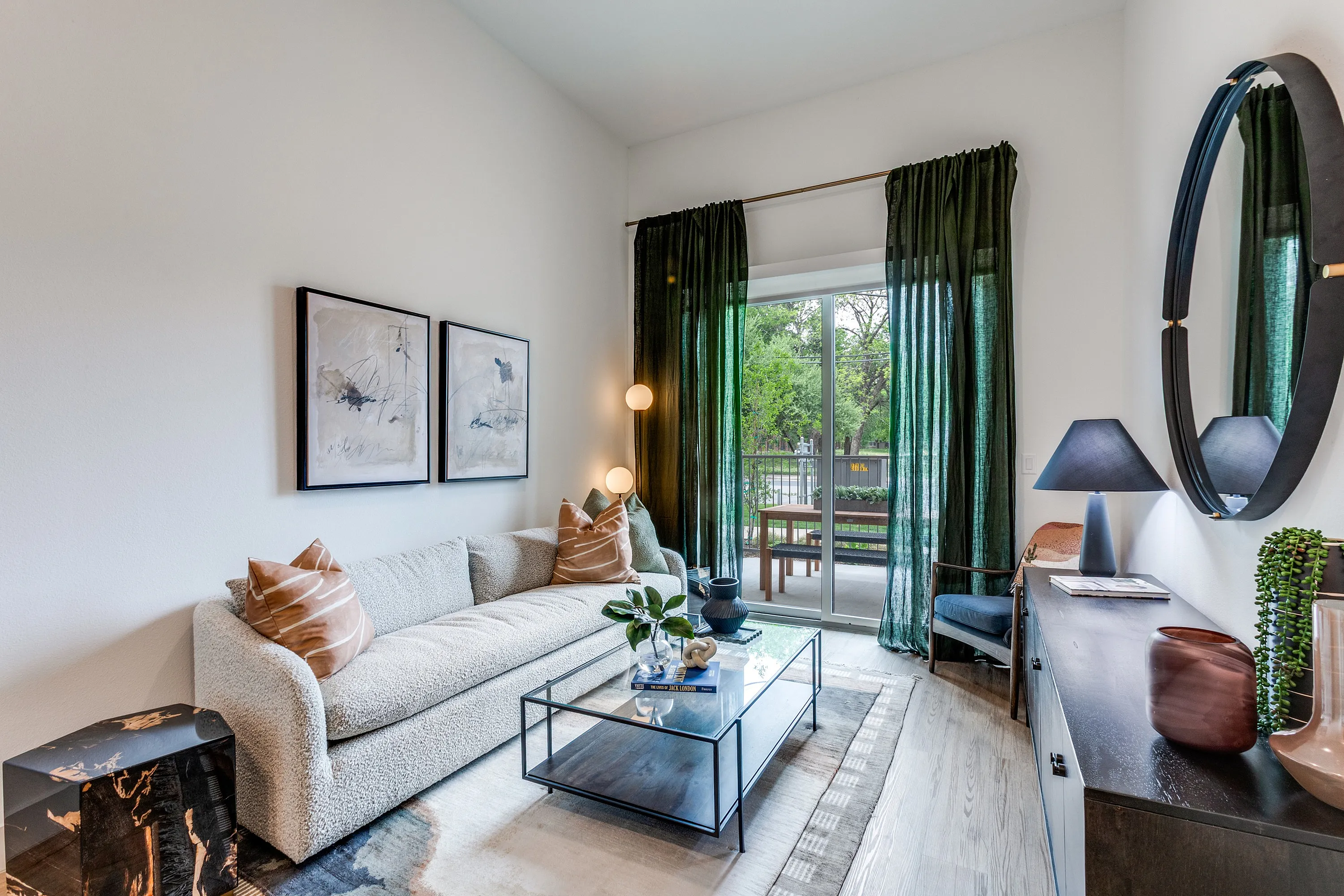 Elegant living room with chic decor, plush sofa, and glass coffee table, leading to a scenic balcony view through glass doors.