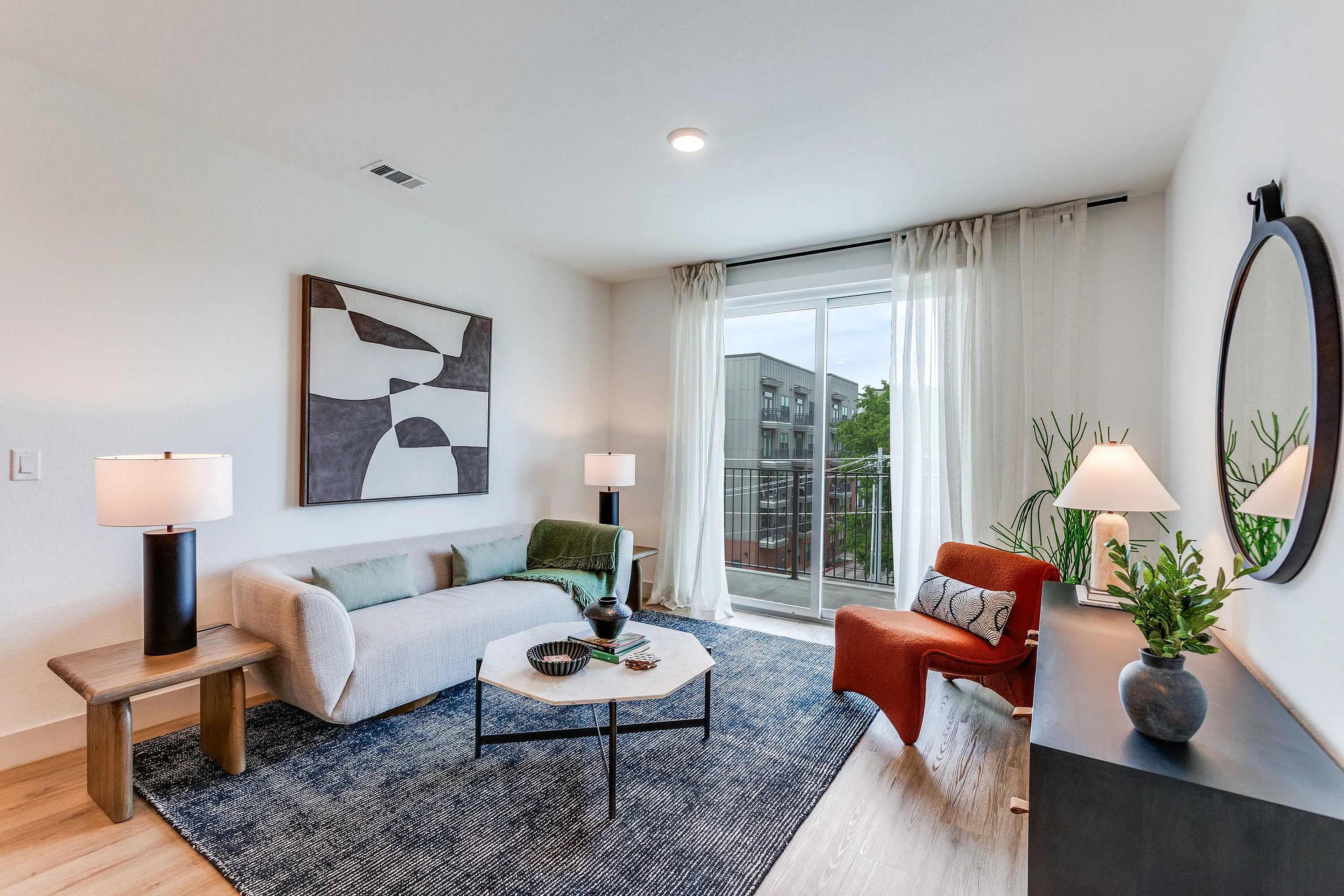 Chic and modern living room with stylish decor, featuring a comfortable sofa, elegant artwork, and large windows offering natural light and a balcony view.