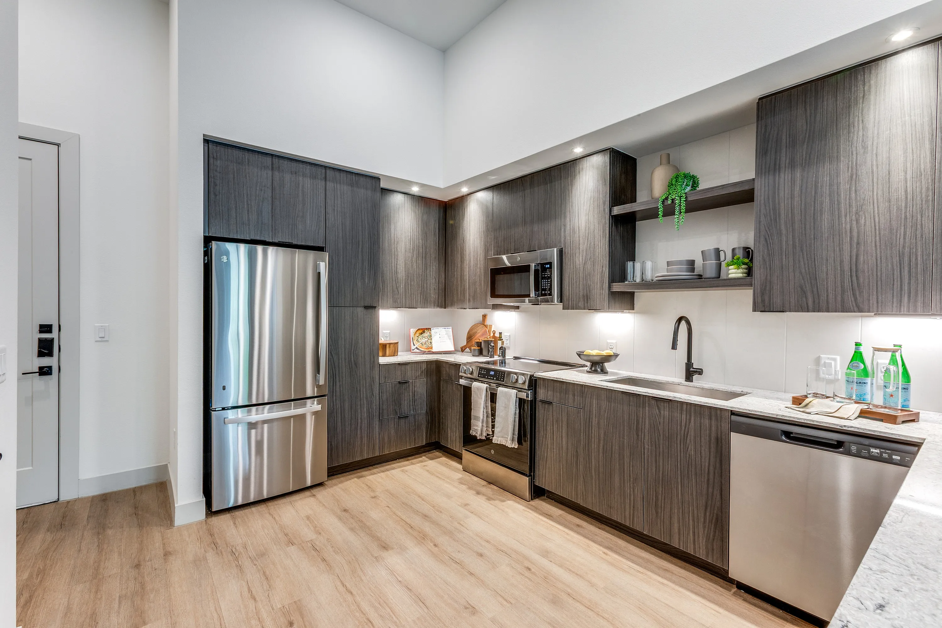 Elegant modern kitchen with sleek stainless steel appliances, dark wood cabinetry, and bright under-cabinet lighting on a stylish wooden floor.